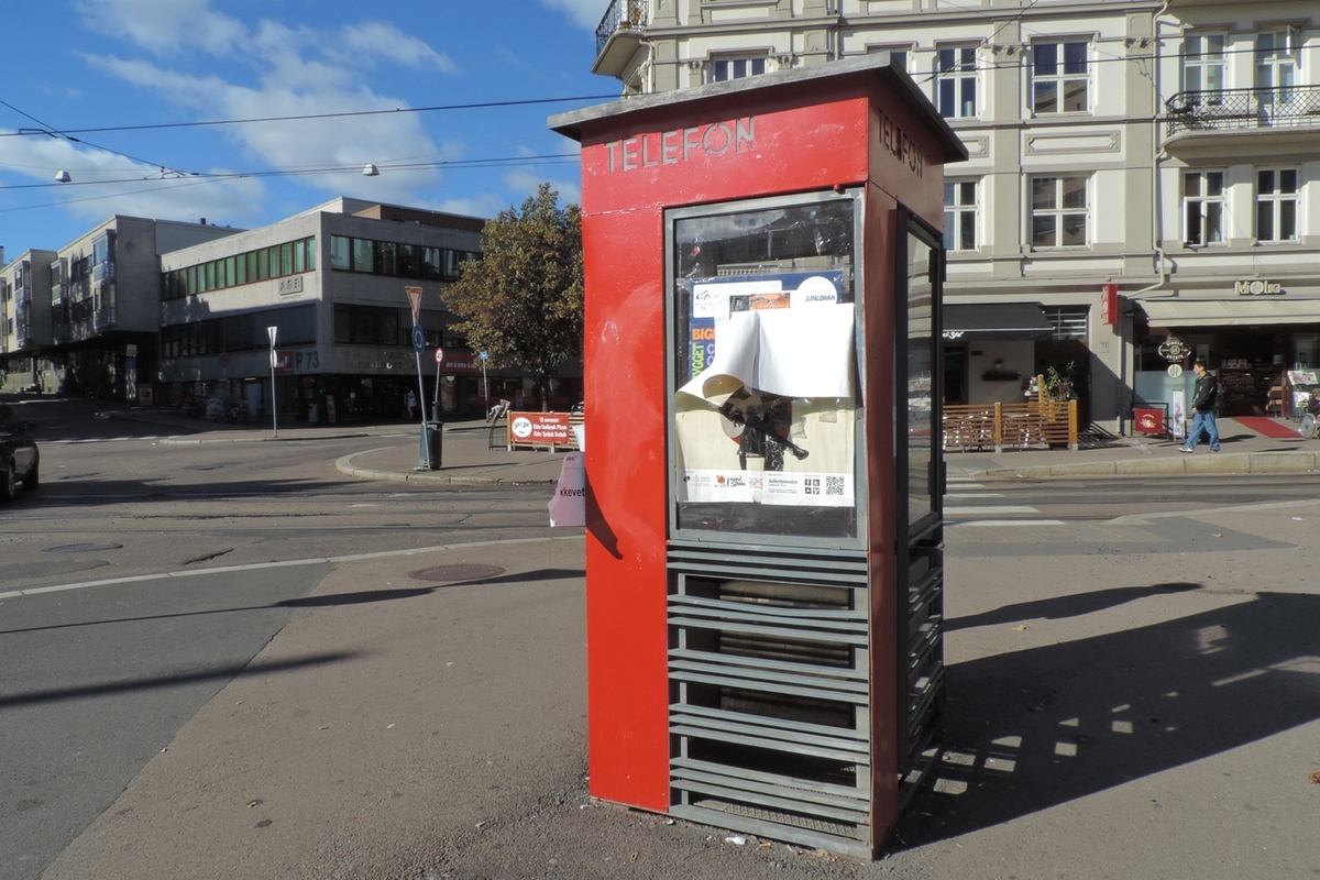 This is the story of how Norway’s most important conversation-space was designed by a young, freshly graduated man from Bergen.

“Norwegian architects are hereby invited…”
In the autumn of 1932, Oslo Telefonanlegginitiated an architectural competition. Finally, Oslo would get its own telephone booth. The city had had so called “talking-stations” from 1885, which in turn were overtaken by automatic telephones 
 only available at selected Narvesen kiosks. The state 
was of the opinion that now was the time to offer the public a better service; public telephone booths open 24/7, like the ones they already had in Sweden and England. But what would they look like, these new telephone booths? What considerations would it
 be necessary to take when designing it? The telegraph board developed a detailed list of demands and restraints: “The booth is intended to be placed outside on the streets and squares and need to be designed so that snow and ice does not hinder the opening and closing of the doors,” they wrote. “To prevent vandalism, theft, uncleanliness etc. inside the booth, it needs to be designed so that from all angles one may see what is going on in there.” Additionally, it would need to withstand storms and bad weather, and “preferably also being whipped by rain mixed with seawater” 

This was not all: The appearance would have to be «pleasing». The booth also needed to be movable, so that it could be taken in to be serviced at Telegrafverket’s main workshops. The reqired material was iron, and the surface was to be spray painted  preferably using car-body paint. There was a requirement for “a writing shelf, a pack shelf, and a suitable place for the telephone catalogue.” Also, there would need to be an illuminated TELEFON  sign, easily visible from all four angles. The total cost for each booth should not exceed 1000 kroner. The first prize for coming up with such a product was 800 kroner.

“Norwegianarchitects are hereby invited to partake in a competition for the design of a telephone booth…”  

The man with the solution
«At some point in 1932, Georg Fredrik sat at a party in Bergen. Maybe he felt a bit lost and forgotten as he often had throughout his life. He retreated to a quiet corner, took out a pencil and strted doodling on a matchbox.  According to my mother, this was how the telephone booth came into being.” In the book “Norges lille røde  historien om telefonkiosken,” Lars Fasting describes his father, the man who is far less known than the iconic architctural structure he left behind. Georg Fredrik Fasting was from Bergen, born into a family of working people and smallholders. One unusual facet of Georg Fredrik was that he was born without ears. His mother made sure he learnt to speak, read and write, 
ut Lars Fasting indicates that his father would seek refuge in drawing when the social challenges became too much to bear. And in the end drawing became his profession. In 1924 he secured a guarantor for a student loan, and started studying to become an a
rchitect at the NTH. Throughout the 1930s he entered several architectural competitions, with drafts produced, according to his son, “after work and in the late hours of the night.”

His efforts were not wasted. Out of 93 entries, with names such as “Flirt”, “Brrr”, “Ring” and “Amor”, the jury selected Fasting’s submission, “RIKS” as the new telephone booth: “The draft shows a strikingly simple solution to the task, technically as well as aesthetically well worked out.”

Taut and provident
Simple and aesthetc are the keywords here. Fasting had designed a booth pointing towards the future, and to modernism. Just how modern it was can be seen by comparing RIKS to the British telephone booth, also designed in the interwar-era. While the British version with it classicistic style is looking back to the heyday of the empire, Fasting’s booth is progressive and functionalistic. Like most Norwegian architects, Fasting broke with the classicistic style of architecture after the Stockholm-exhibition in 1930. “After it, almost all buildings erected in Norway until the German invasion in 1940, were in the functionalistic architectural style,” writes senior curator of architecture at the Norwegian National Museum, Ulf Grønvold, in the book, “Den lille røde”.“TheNorwegian booth is a piece of functionalistic architecture, an asymmetric composition with its roof slab overhanging the word TELEFON, in bold sans seraph lettering,”concludes Ulf Grønvold.

Fashionably red
And it was red. Fasting chose a colour which was part of the modern palette. “A bright red colour, but not as shiny as a signal red, the character of the colour places it among the fashionable colours within functionalism,” states paintings conservator and researcher in NIKU (Norwegian Institute for Cultural Heitage Research), Jon Brænne. In his opinion, Fasting went for visibility without making the booth stand out too much from its surroundings. The original colour was in use up to around 1950, when it changed to signal red. Towards the end of the 1970s the clour was again adjusted towards today’s orangey red.

The design, however, has not changed. RIKS is eighty years and still looks remarkably good. That’s what makes Fasting’s telephone booth a classic  even before it was added to DOCOMOMO’s list over moden icons of design. For Telenor, the telephone booth has served as a pathway into the hearts of the public. For many, Telenor (Televerket) was synonymous with exactly this telephone booth, because this was where one would go to place a call. Having a home
phone was not common until the 1980s. As such the red box became part of the Norwegian everyday and consciousness. The symbol- and publicity value of this is hard to evaluate, but in 2007 it was time to give honour where honour was due, Telenor, in consul
tation with the Directorate for Cultural Heritage, decided to preserve 100 telephone booths for all eternity.

And what about Georg Fredrik Fasting? What happened to him? At the age of 56 an entry in his diary states: «I CAN HEAR». As the first person in th world he had undergone an operation where he had ear canals constructed and eardrums fitted. For the rest of his life, the man behind Norway’s own telephone booth could answer the telephone himself.

Source: Norges lille røde historien om telefonkiosken (2007), issued by The Norwegian Telecom Museum and Telenor Cultural Heritage.