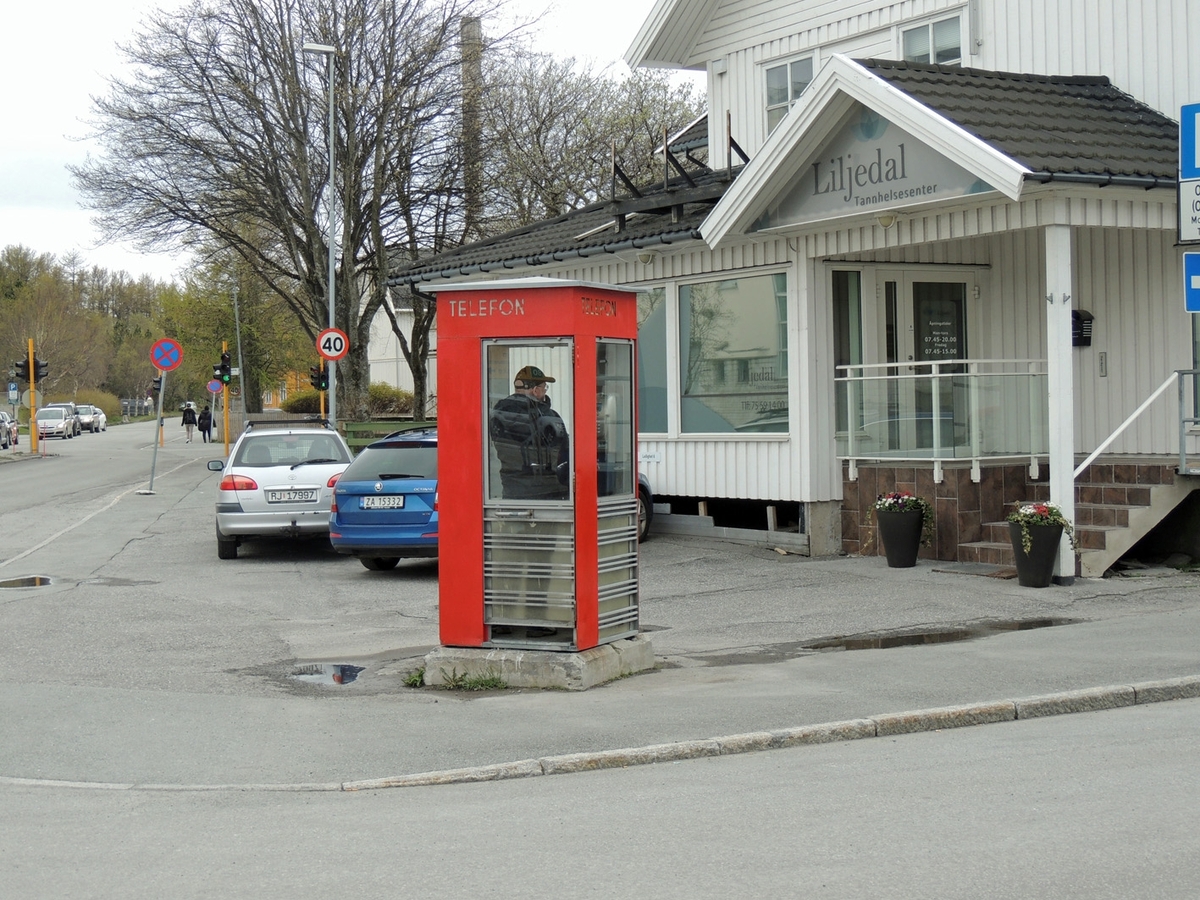 This is the story of how Norway’s most important conversation-space was designed by a young, freshly graduated man from Bergen.

“Norwegian architects are hereby invited…”
In the autumn of 1932, Oslo Telefonanlegginitiated an architectural competition. Finally, Oslo would get its own telephone booth. The city had had so called “talking-stations” from 1885, which in turn were overtaken by automatic telephones 
 only available at selected Narvesen kiosks. The state 
was of the opinion that now was the time to offer the public a better service; public telephone booths open 24/7, like the ones they already had in Sweden and England. But what would they look like, these new telephone booths? What considerations would it
 be necessary to take when designing it? The telegraph board developed a detailed list of demands and restraints: “The booth is intended to be placed outside on the streets and squares and need to be designed so that snow and ice does not hinder the opening and closing of the doors,” they wrote. “To prevent vandalism, theft, uncleanliness etc. inside the booth, it needs to be designed so that from all angles one may see what is going on in there.” Additionally, it would need to withstand storms and bad weather, and “preferably also being whipped by rain mixed with seawater” 

This was not all: The appearance would have to be «pleasing». The booth also needed to be movable, so that it could be taken in to be serviced at Telegrafverket’s main workshops. The reqired material was iron, and the surface was to be spray painted  preferably using car-body paint. There was a requirement for “a writing shelf, a pack shelf, and a suitable place for the telephone catalogue.” Also, there would need to be an illuminated TELEFON  sign, easily visible from all four angles. The total cost for each booth should not exceed 1000 kroner. The first prize for coming up with such a product was 800 kroner.

“Norwegianarchitects are hereby invited to partake in a competition for the design of a telephone booth…”  

The man with the solution
«At some point in 1932, Georg Fredrik sat at a party in Bergen. Maybe he felt a bit lost and forgotten as he often had throughout his life. He retreated to a quiet corner, took out a pencil and strted doodling on a matchbox.  According to my mother, this was how the telephone booth came into being.” In the book “Norges lille røde  historien om telefonkiosken,” Lars Fasting describes his father, the man who is far less known than the iconic architctural structure he left behind. Georg Fredrik Fasting was from Bergen, born into a family of working people and smallholders. One unusual facet of Georg Fredrik was that he was born without ears. His mother made sure he learnt to speak, read and write, 
ut Lars Fasting indicates that his father would seek refuge in drawing when the social challenges became too much to bear. And in the end drawing became his profession. In 1924 he secured a guarantor for a student loan, and started studying to become an a
rchitect at the NTH. Throughout the 1930s he entered several architectural competitions, with drafts produced, according to his son, “after work and in the late hours of the night.”

His efforts were not wasted. Out of 93 entries, with names such as “Flirt”, “Brrr”, “Ring” and “Amor”, the jury selected Fasting’s submission, “RIKS” as the new telephone booth: “The draft shows a strikingly simple solution to the task, technically as well as aesthetically well worked out.”

Taut and provident
Simple and aesthetc are the keywords here. Fasting had designed a booth pointing towards the future, and to modernism. Just how modern it was can be seen by comparing RIKS to the British telephone booth, also designed in the interwar-era. While the British version with it classicistic style is looking back to the heyday of the empire, Fasting’s booth is progressive and functionalistic. Like most Norwegian architects, Fasting broke with the classicistic style of architecture after the Stockholm-exhibition in 1930. “After it, almost all buildings erected in Norway until the German invasion in 1940, were in the functionalistic architectural style,” writes senior curator of architecture at the Norwegian National Museum, Ulf Grønvold, in the book, “Den lille røde”.“TheNorwegian booth is a piece of functionalistic architecture, an asymmetric composition with its roof slab overhanging the word TELEFON, in bold sans seraph lettering,”concludes Ulf Grønvold.

Fashionably red
And it was red. Fasting chose a colour which was part of the modern palette. “A bright red colour, but not as shiny as a signal red, the character of the colour places it among the fashionable colours within functionalism,” states paintings conservator and researcher in NIKU (Norwegian Institute for Cultural Heitage Research), Jon Brænne. In his opinion, Fasting went for visibility without making the booth stand out too much from its surroundings. The original colour was in use up to around 1950, when it changed to signal red. Towards the end of the 1970s the clour was again adjusted towards today’s orangey red.

The design, however, has not changed. RIKS is eighty years and still looks remarkably good. That’s what makes Fasting’s telephone booth a classic  even before it was added to DOCOMOMO’s list over moden icons of design. For Telenor, the telephone booth has served as a pathway into the hearts of the public. For many, Telenor (Televerket) was synonymous with exactly this telephone booth, because this was where one would go to place a call. Having a home
phone was not common until the 1980s. As such the red box became part of the Norwegian everyday and consciousness. The symbol- and publicity value of this is hard to evaluate, but in 2007 it was time to give honour where honour was due, Telenor, in consul
tation with the Directorate for Cultural Heritage, decided to preserve 100 telephone booths for all eternity.

And what about Georg Fredrik Fasting? What happened to him? At the age of 56 an entry in his diary states: «I CAN HEAR». As the first person in th world he had undergone an operation where he had ear canals constructed and eardrums fitted. For the rest of his life, the man behind Norway’s own telephone booth could answer the telephone himself.

Source: Norges lille røde historien om telefonkiosken (2007), issued by The Norwegian Telecom Museum and Telenor Cultural Heritage.