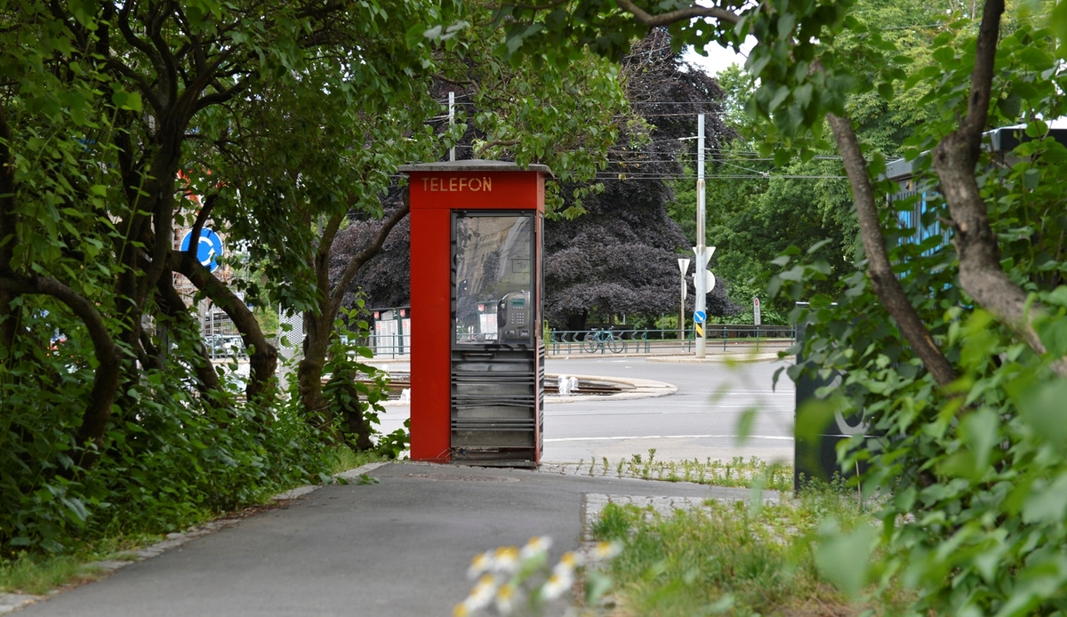 This is the story of how Norway’s most important conversation-space was designed by a young, freshly graduated man from Bergen.

“Norwegian architects are hereby invited…”
In the autumn of 1932, Oslo Telefonanlegginitiated an architectural competition. Finally, Oslo would get its own telephone booth. The city had had so called “talking-stations” from 1885, which in turn were overtaken by automatic telephones 
 only available at selected Narvesen kiosks. The state 
was of the opinion that now was the time to offer the public a better service; public telephone booths open 24/7, like the ones they already had in Sweden and England. But what would they look like, these new telephone booths? What considerations would it
 be necessary to take when designing it? The telegraph board developed a detailed list of demands and restraints: “The booth is intended to be placed outside on the streets and squares and need to be designed so that snow and ice does not hinder the opening and closing of the doors,” they wrote. “To prevent vandalism, theft, uncleanliness etc. inside the booth, it needs to be designed so that from all angles one may see what is going on in there.” Additionally, it would need to withstand storms and bad weather, and “preferably also being whipped by rain mixed with seawater” 

This was not all: The appearance would have to be «pleasing». The booth also needed to be movable, so that it could be taken in to be serviced at Telegrafverket’s main workshops. The reqired material was iron, and the surface was to be spray painted  preferably using car-body paint. There was a requirement for “a writing shelf, a pack shelf, and a suitable place for the telephone catalogue.” Also, there would need to be an illuminated TELEFON  sign, easily visible from all four angles. The total cost for each booth should not exceed 1000 kroner. The first prize for coming up with such a product was 800 kroner.

“Norwegianarchitects are hereby invited to partake in a competition for the design of a telephone booth…”  

The man with the solution
«At some point in 1932, Georg Fredrik sat at a party in Bergen. Maybe he felt a bit lost and forgotten as he often had throughout his life. He retreated to a quiet corner, took out a pencil and strted doodling on a matchbox.  According to my mother, this was how the telephone booth came into being.” In the book “Norges lille røde  historien om telefonkiosken,” Lars Fasting describes his father, the man who is far less known than the iconic architctural structure he left behind. Georg Fredrik Fasting was from Bergen, born into a family of working people and smallholders. One unusual facet of Georg Fredrik was that he was born without ears. His mother made sure he learnt to speak, read and write, 
ut Lars Fasting indicates that his father would seek refuge in drawing when the social challenges became too much to bear. And in the end drawing became his profession. In 1924 he secured a guarantor for a student loan, and started studying to become an a
rchitect at the NTH. Throughout the 1930s he entered several architectural competitions, with drafts produced, according to his son, “after work and in the late hours of the night.”

His efforts were not wasted. Out of 93 entries, with names such as “Flirt”, “Brrr”, “Ring” and “Amor”, the jury selected Fasting’s submission, “RIKS” as the new telephone booth: “The draft shows a strikingly simple solution to the task, technically as well as aesthetically well worked out.”

Taut and provident
Simple and aesthetc are the keywords here. Fasting had designed a booth pointing towards the future, and to modernism. Just how modern it was can be seen by comparing RIKS to the British telephone booth, also designed in the interwar-era. While the British version with it classicistic style is looking back to the heyday of the empire, Fasting’s booth is progressive and functionalistic. Like most Norwegian architects, Fasting broke with the classicistic style of architecture after the Stockholm-exhibition in 1930. “After it, almost all buildings erected in Norway until the German invasion in 1940, were in the functionalistic architectural style,” writes senior curator of architecture at the Norwegian National Museum, Ulf Grønvold, in the book, “Den lille røde”.“TheNorwegian booth is a piece of functionalistic architecture, an asymmetric composition with its roof slab overhanging the word TELEFON, in bold sans seraph lettering,”concludes Ulf Grønvold.

Fashionably red
And it was red. Fasting chose a colour which was part of the modern palette. “A bright red colour, but not as shiny as a signal red, the character of the colour places it among the fashionable colours within functionalism,” states paintings conservator and researcher in NIKU (Norwegian Institute for Cultural Heitage Research), Jon Brænne. In his opinion, Fasting went for visibility without making the booth stand out too much from its surroundings. The original colour was in use up to around 1950, when it changed to signal red. Towards the end of the 1970s the clour was again adjusted towards today’s orangey red.

The design, however, has not changed. RIKS is eighty years and still looks remarkably good. That’s what makes Fasting’s telephone booth a classic  even before it was added to DOCOMOMO’s list over moden icons of design. For Telenor, the telephone booth has served as a pathway into the hearts of the public. For many, Telenor (Televerket) was synonymous with exactly this telephone booth, because this was where one would go to place a call. Having a home
phone was not common until the 1980s. As such the red box became part of the Norwegian everyday and consciousness. The symbol- and publicity value of this is hard to evaluate, but in 2007 it was time to give honour where honour was due, Telenor, in consul
tation with the Directorate for Cultural Heritage, decided to preserve 100 telephone booths for all eternity.

And what about Georg Fredrik Fasting? What happened to him? At the age of 56 an entry in his diary states: «I CAN HEAR». As the first person in th world he had undergone an operation where he had ear canals constructed and eardrums fitted. For the rest of his life, the man behind Norway’s own telephone booth could answer the telephone himself.

Source: Norges lille røde historien om telefonkiosken (2007), issued by The Norwegian Telecom Museum and Telenor Cultural Heritage.