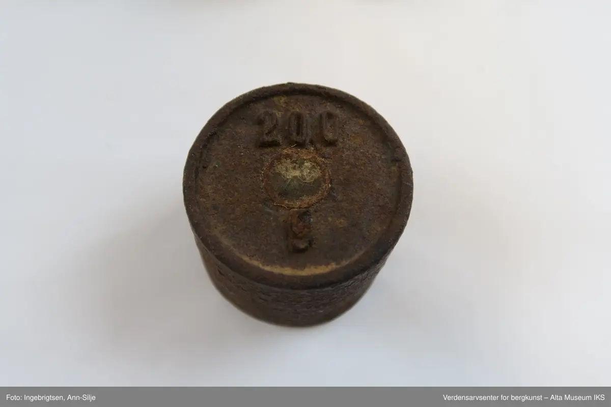 Rektangulær trebit, med hull tilpasset ulike loddstørrelser. Det er 7 lodd: 2 stk. 10 gram, 1 stk. 20 gram, 1 st. 50 gram, 2 stk. 100 gram og 1 stk. 200 gram. Alle loddene er sylinderformet med knott på toppen. Loddene varierer i størrelse: de minste er 2 cm i diameter og 1 cm i høyde, mens den største er 4 cm i diameter og 2,8 cm i høyde.