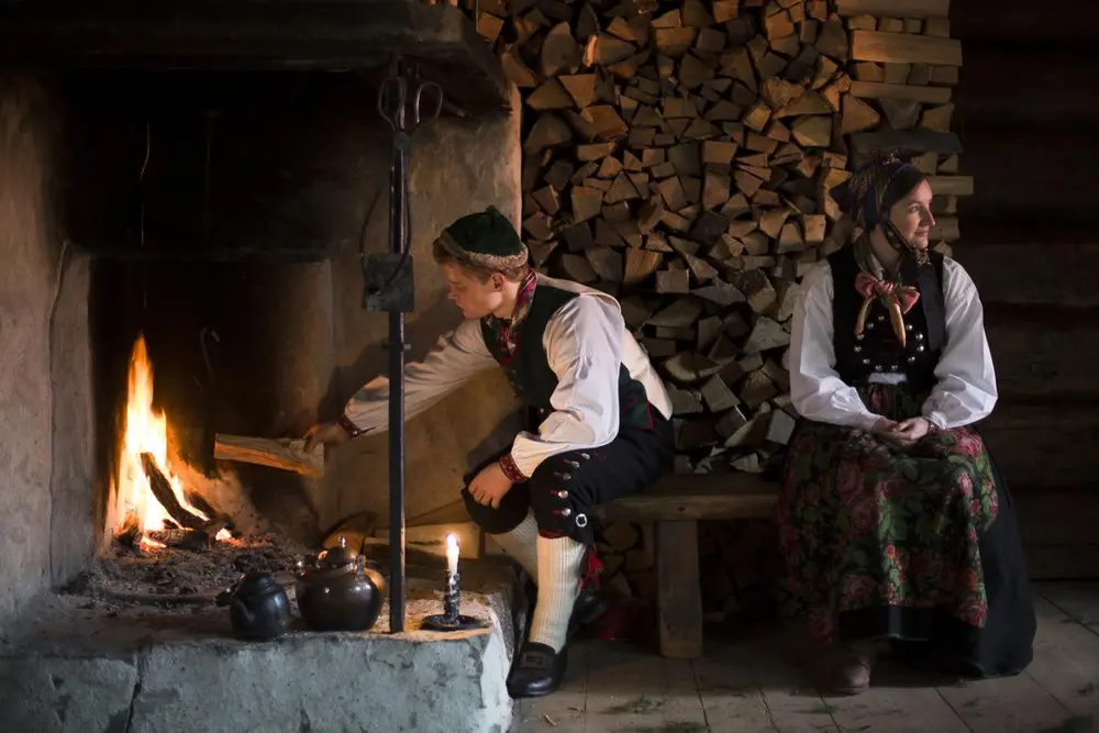 Mann og kvinne i folkedrakt sitter foran grua