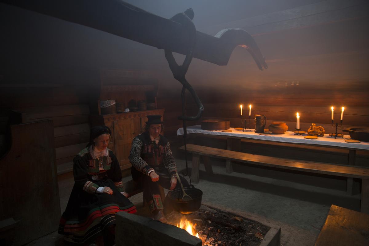 Julepyntet årestue. To personer i bunad sitter ved åren.