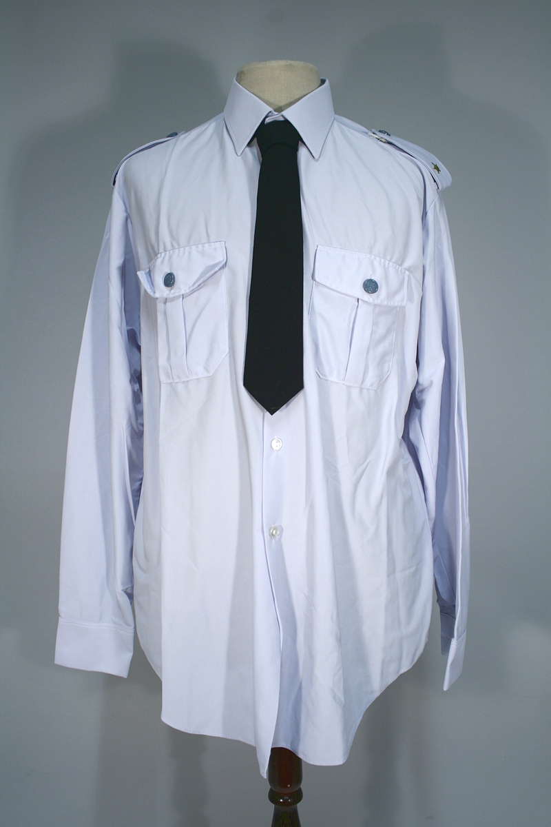 Lang grå uniformsfrakk, grå uniformsjakke, grå vinterlue (båtlue) med for i fuskepels, sort slips, grå uniformslue med blank sort skjerm og regntrekk, tre lyseblå uniformsskjorter. Uniformen har skulderklaffer med en gullstjerne, altså distinksjon for førstebetjent. Plasknapper med valknuten. Luene er forsynt med metallmerker i gull og rødt, den norske krone over valknuten som var symbolet for kriminalomsorgen i perioden 1964-2001.