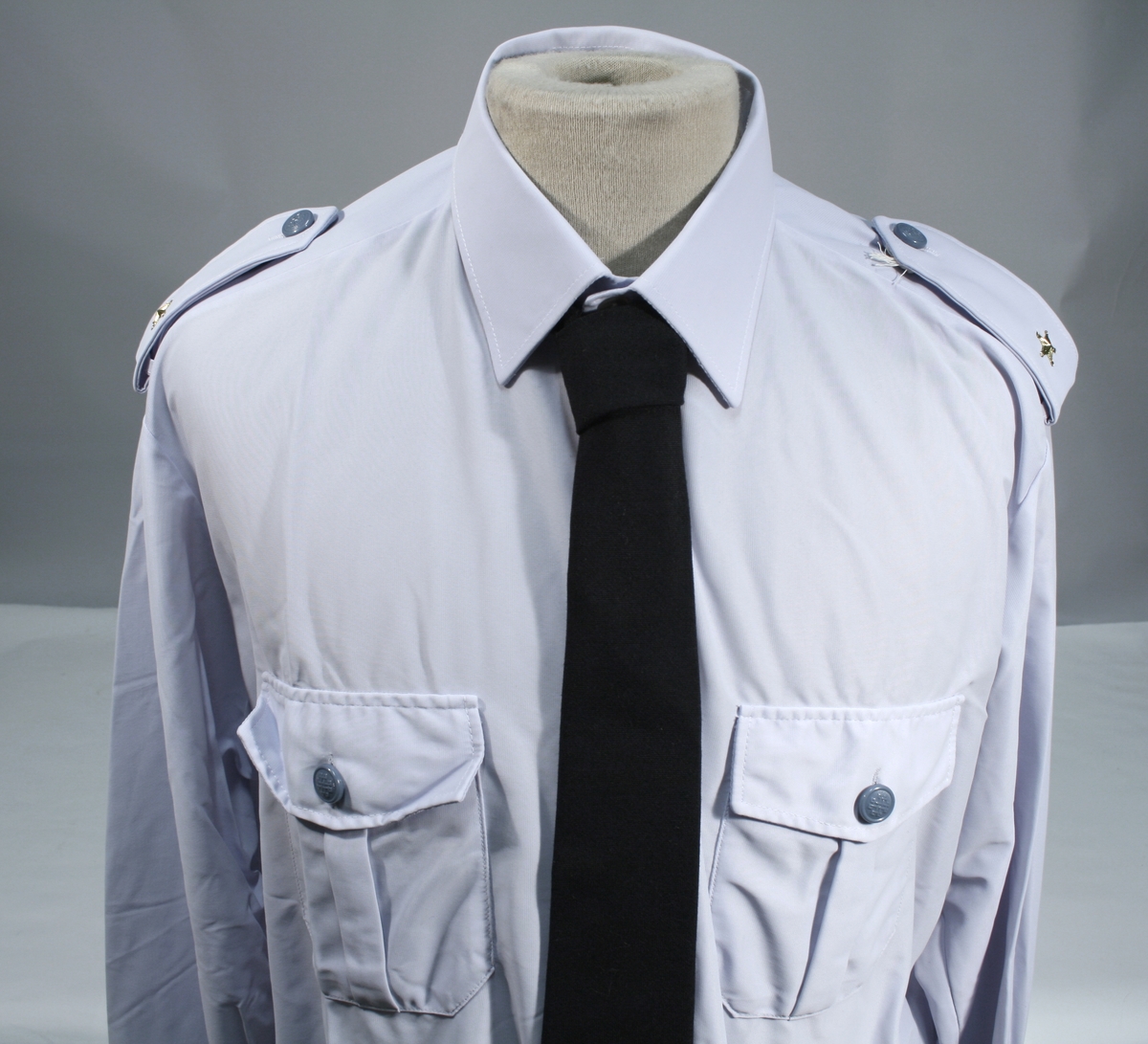 Lang grå uniformsfrakk, grå uniformsjakke, grå vinterlue (båtlue) med for i fuskepels, sort slips, grå uniformslue med blank sort skjerm og regntrekk, tre lyseblå uniformsskjorter. Uniformen har skulderklaffer med en gullstjerne, altså distinksjon for førstebetjent. Plasknapper med valknuten. Luene er forsynt med metallmerker i gull og rødt, den norske krone over valknuten som var symbolet for kriminalomsorgen i perioden 1964-2001.