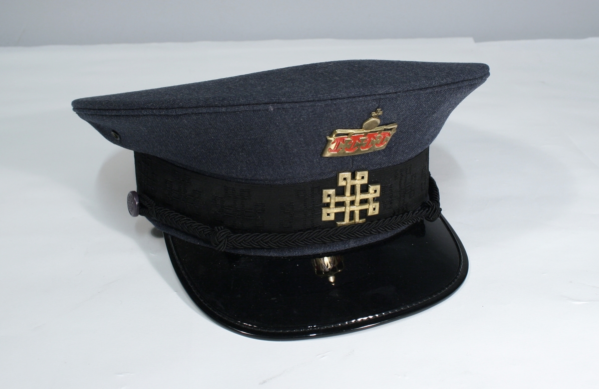 Lang grå uniformsfrakk, grå uniformsjakke, grå vinterlue (båtlue) med for i fuskepels, sort slips, grå uniformslue med blank sort skjerm og regntrekk, tre lyseblå uniformsskjorter. Uniformen har skulderklaffer med en gullstjerne, altså distinksjon for førstebetjent. Plasknapper med valknuten. Luene er forsynt med metallmerker i gull og rødt, den norske krone over valknuten som var symbolet for kriminalomsorgen i perioden 1964-2001.