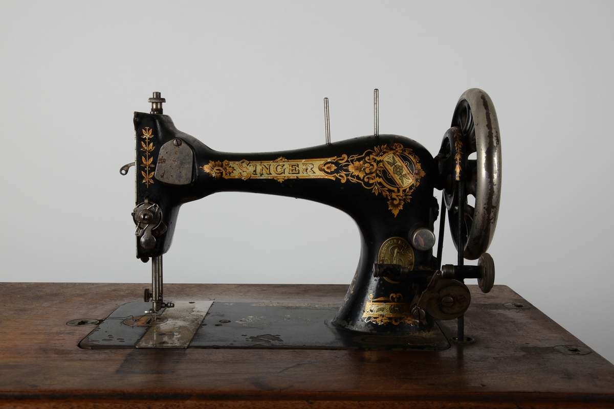 Symaskin med bord og lokk. Understell av støpejern, med pedal.

Treflaten som symaskinen står på har innfelte hull til å sette lokket i. En liten trebit står i et hull i bordet.