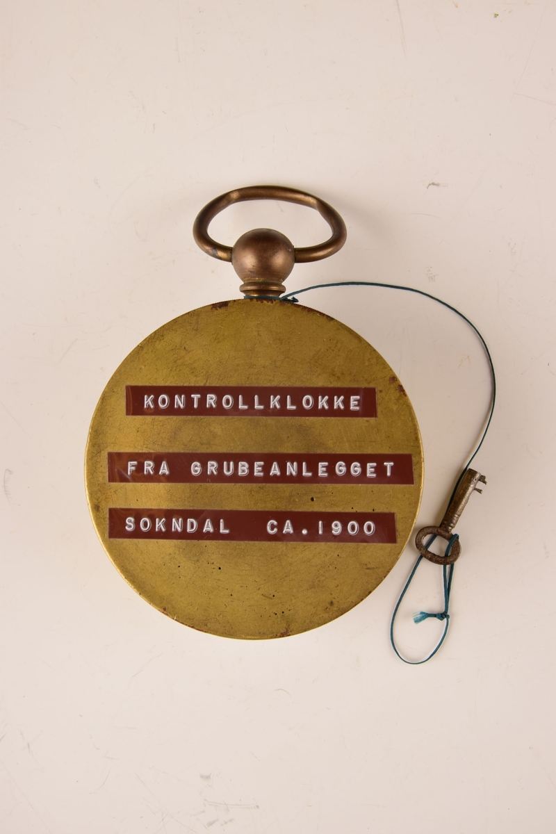 Kontrollklokke med nøkkel.

Hengslet lokk. Åpnes til måleskive av papir, med viser skrudd fast til korpus. Måleskiven kan roteres via midtmekanismen. Nøkkelen er festet til klokken med en snor. Håndtak/hank i topp.
