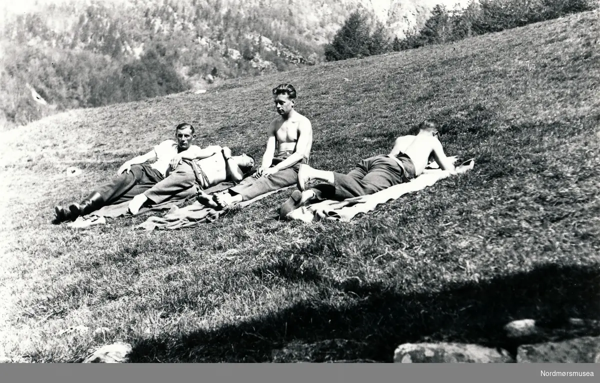 Fire menn som ligger på gresset og soler seg i finværet.