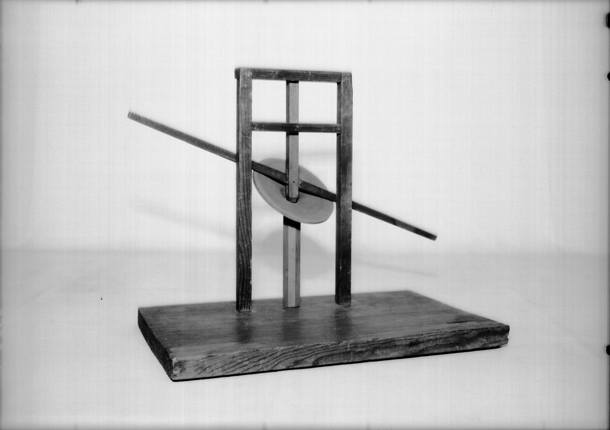 Modell ur Polhems mekaniska alfabet. Text på föremålet: "LXIV". Vid rotation av den lodräta axeln erhålles med hjälp av den vinkelställda skivan en vickande rörelse hos armen.