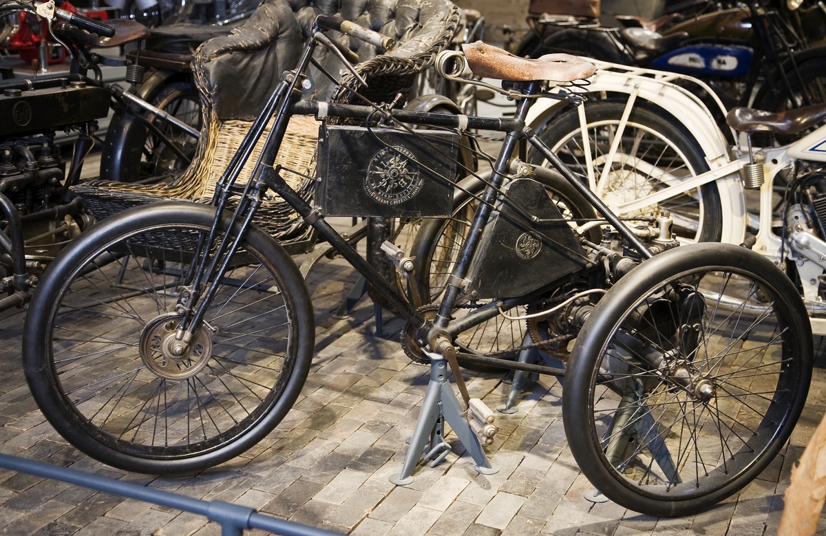 Trehjulig motorcykel med motorn placerad mellan bakhjulen. Kraften överförs från motorn till bakaxeln med kugghjul. Bandbroms på bakaxelns differential och på framhjulets nav. Cudell & Cie, Aachen ytförgasare. Batteritändning till tändstift, torrcellbatteriet i lådan på det horisontella ramröret. Reglaget vid styret är handtag till fram och bakbroms. Reglage vid ramen till luftintag på tanken (2 st). 
Museets exemplar har haft en smidd "ögla" för påhängsvagn.  Encylindrig luftkyld fyrtakts bensinmotor, cylindervolym 239 cc, cylinderdiameter 62 mm Slaglängd 70 mm 1 ¾ hk vid 1500 varv/minut Högsta fart cirka 45 km/tim Hastighetsreglering genom tändningen. Motorns vikt:  18 kg.