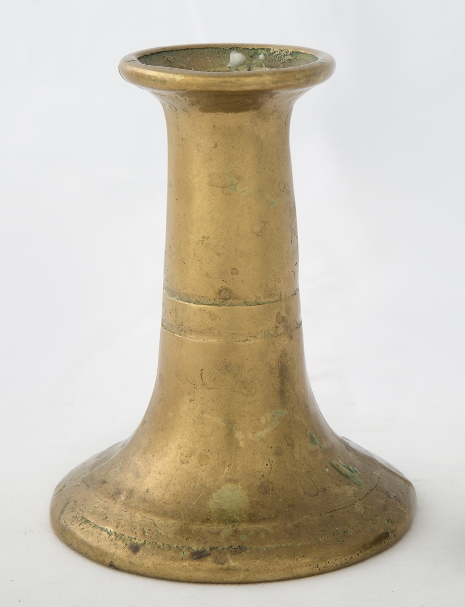 Rund sokkel, slank utføring. Dekorert med to riller på sokkel, og to riller på skaftet. Vider seg ut ved lyspipen.