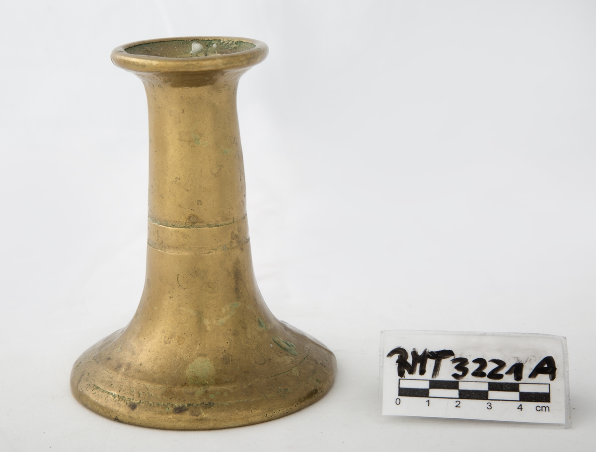 Rund sokkel, slank utføring. Dekorert med to riller på sokkel, og to riller på skaftet. Vider seg ut ved lyspipen.