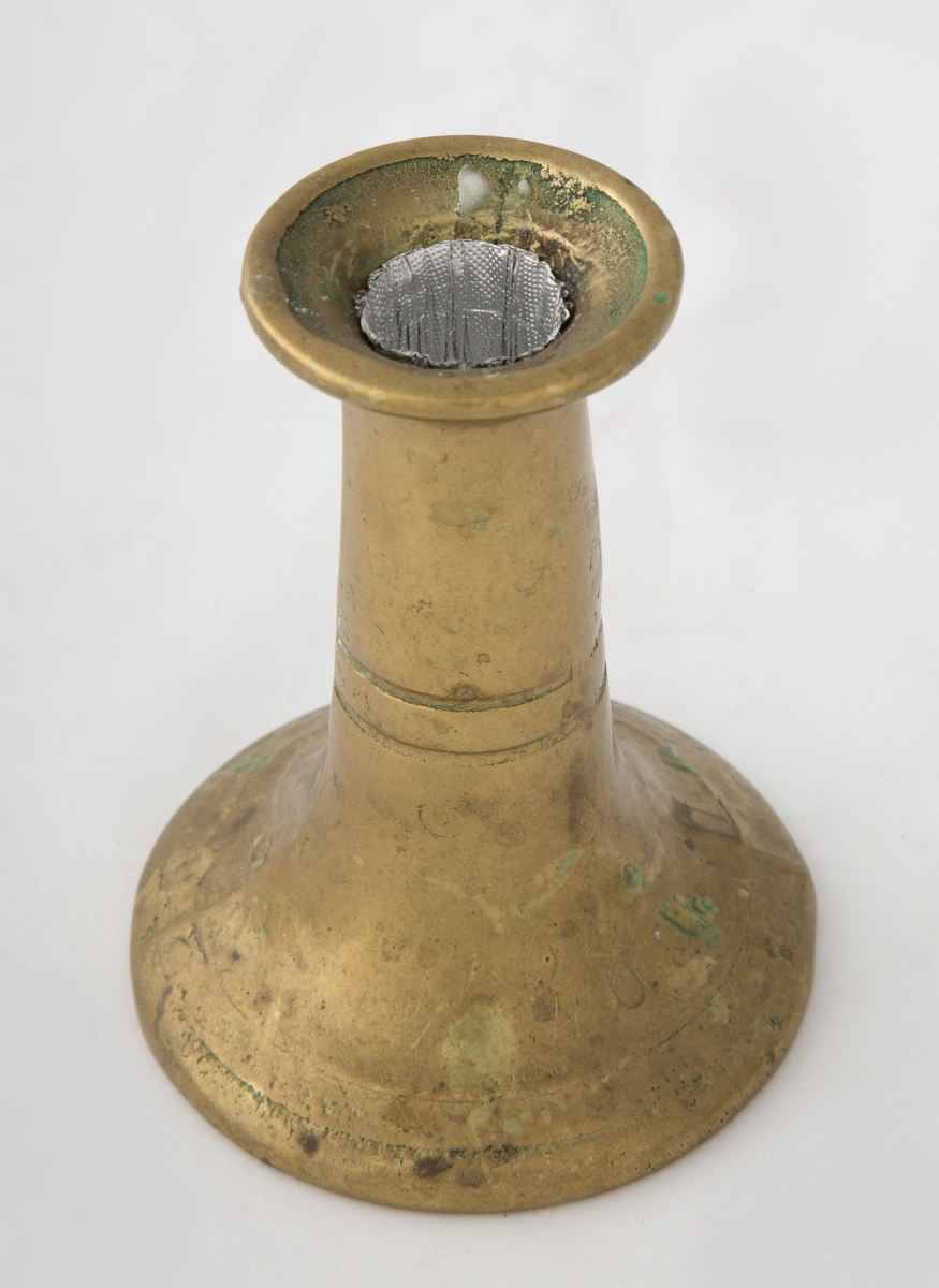 Rund sokkel, slank utføring. Dekorert med to riller på sokkel, og to riller på skaftet. Vider seg ut ved lyspipen.