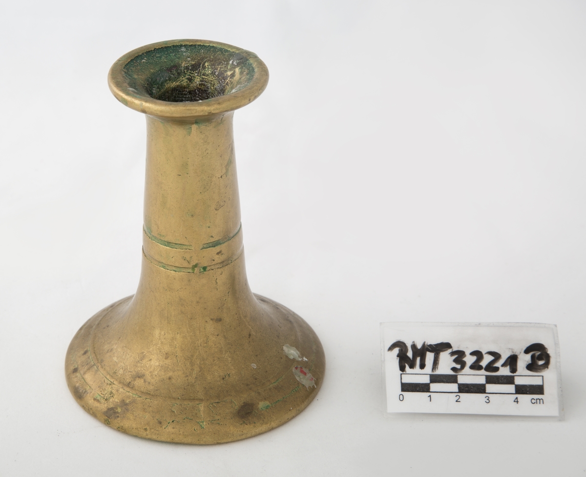 Rund sokkel, slank utføring. Dekorert med to riller på sokkel, og to riller på skaftet. Vider seg ut ved lyspipen.