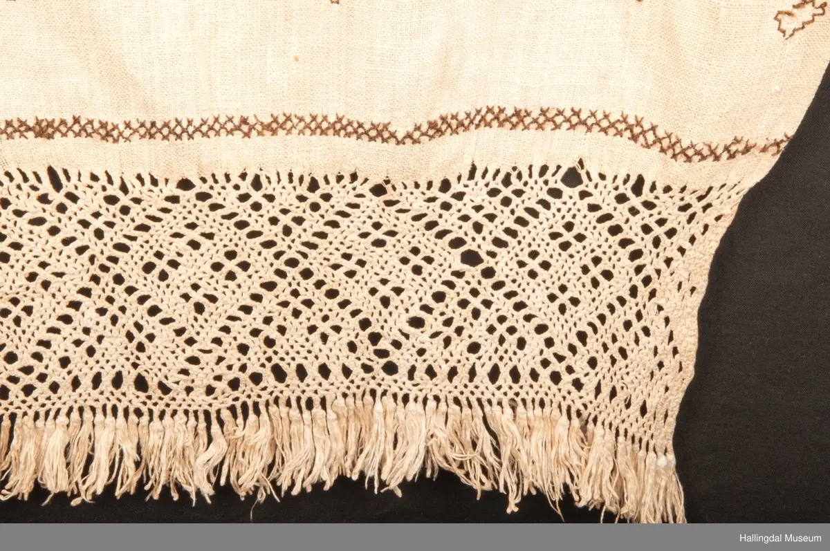 Tilnærmet rektangulært stk. hvit linlerret, håndvevet. Jarekanter i langsidene, faldet for hånd i ei kortside. Det vevde stykket ca. 130 cm langt og fortsetter i en knipling i firflettingsteknikk av renningstrådene. På linet er brodert mønster m/ 2-tråds, håndspunnet, mørk brunt ullgarn. Geometriske mønster i holbeinsting og korssting, nær falden er brodert 3 bokstaver (siste er D, to første er usikre) og årstallet 1757 i korssting og kjedessting.