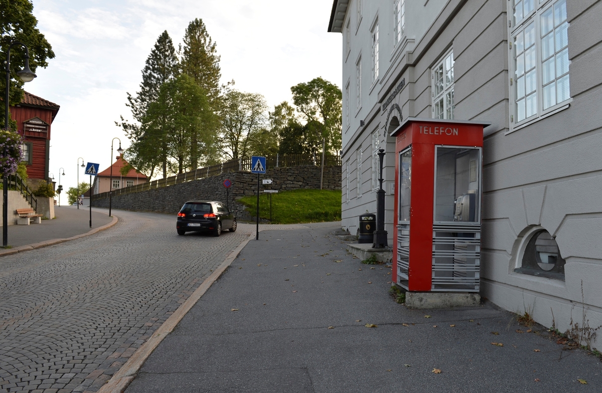 This is the story of how Norway’s most important conversation-space was designed by a young, freshly graduated man from Bergen.

“Norwegian architects are hereby invited…”
In the autumn of 1932, Oslo Telefonanlegginitiated an architectural competition. Finally, Oslo would get its own telephone booth. The city had had so called “talking-stations” from 1885, which in turn were overtaken by automatic telephones 
 only available at selected Narvesen kiosks. The state 
was of the opinion that now was the time to offer the public a better service; public telephone booths open 24/7, like the ones they already had in Sweden and England. But what would they look like, these new telephone booths? What considerations would it
 be necessary to take when designing it? The telegraph board developed a detailed list of demands and restraints: “The booth is intended to be placed outside on the streets and squares and need to be designed so that snow and ice does not hinder the opening and closing of the doors,” they wrote. “To prevent vandalism, theft, uncleanliness etc. inside the booth, it needs to be designed so that from all angles one may see what is going on in there.” Additionally, it would need to withstand storms and bad weather, and “preferably also being whipped by rain mixed with seawater” 

This was not all: The appearance would have to be «pleasing». The booth also needed to be movable, so that it could be taken in to be serviced at Telegrafverket’s main workshops. The reqired material was iron, and the surface was to be spray painted  preferably using car-body paint. There was a requirement for “a writing shelf, a pack shelf, and a suitable place for the telephone catalogue.” Also, there would need to be an illuminated TELEFON  sign, easily visible from all four angles. The total cost for each booth should not exceed 1000 kroner. The first prize for coming up with such a product was 800 kroner.

“Norwegianarchitects are hereby invited to partake in a competition for the design of a telephone booth…”  

The man with the solution
«At some point in 1932, Georg Fredrik sat at a party in Bergen. Maybe he felt a bit lost and forgotten as he often had throughout his life. He retreated to a quiet corner, took out a pencil and strted doodling on a matchbox.  According to my mother, this was how the telephone booth came into being.” In the book “Norges lille røde  historien om telefonkiosken,” Lars Fasting describes his father, the man who is far less known than the iconic architctural structure he left behind. Georg Fredrik Fasting was from Bergen, born into a family of working people and smallholders. One unusual facet of Georg Fredrik was that he was born without ears. His mother made sure he learnt to speak, read and write, 
ut Lars Fasting indicates that his father would seek refuge in drawing when the social challenges became too much to bear. And in the end drawing became his profession. In 1924 he secured a guarantor for a student loan, and started studying to become an a
rchitect at the NTH. Throughout the 1930s he entered several architectural competitions, with drafts produced, according to his son, “after work and in the late hours of the night.”

His efforts were not wasted. Out of 93 entries, with names such as “Flirt”, “Brrr”, “Ring” and “Amor”, the jury selected Fasting’s submission, “RIKS” as the new telephone booth: “The draft shows a strikingly simple solution to the task, technically as well as aesthetically well worked out.”

Taut and provident
Simple and aesthetc are the keywords here. Fasting had designed a booth pointing towards the future, and to modernism. Just how modern it was can be seen by comparing RIKS to the British telephone booth, also designed in the interwar-era. While the British version with it classicistic style is looking back to the heyday of the empire, Fasting’s booth is progressive and functionalistic. Like most Norwegian architects, Fasting broke with the classicistic style of architecture after the Stockholm-exhibition in 1930. “After it, almost all buildings erected in Norway until the German invasion in 1940, were in the functionalistic architectural style,” writes senior curator of architecture at the Norwegian National Museum, Ulf Grønvold, in the book, “Den lille røde”.“TheNorwegian booth is a piece of functionalistic architecture, an asymmetric composition with its roof slab overhanging the word TELEFON, in bold sans seraph lettering,”concludes Ulf Grønvold.

Fashionably red
And it was red. Fasting chose a colour which was part of the modern palette. “A bright red colour, but not as shiny as a signal red, the character of the colour places it among the fashionable colours within functionalism,” states paintings conservator and researcher in NIKU (Norwegian Institute for Cultural Heitage Research), Jon Brænne. In his opinion, Fasting went for visibility without making the booth stand out too much from its surroundings. The original colour was in use up to around 1950, when it changed to signal red. Towards the end of the 1970s the clour was again adjusted towards today’s orangey red.

The design, however, has not changed. RIKS is eighty years and still looks remarkably good. That’s what makes Fasting’s telephone booth a classic  even before it was added to DOCOMOMO’s list over moden icons of design. For Telenor, the telephone booth has served as a pathway into the hearts of the public. For many, Telenor (Televerket) was synonymous with exactly this telephone booth, because this was where one would go to place a call. Having a home
phone was not common until the 1980s. As such the red box became part of the Norwegian everyday and consciousness. The symbol- and publicity value of this is hard to evaluate, but in 2007 it was time to give honour where honour was due, Telenor, in consul
tation with the Directorate for Cultural Heritage, decided to preserve 100 telephone booths for all eternity.

And what about Georg Fredrik Fasting? What happened to him? At the age of 56 an entry in his diary states: «I CAN HEAR». As the first person in th world he had undergone an operation where he had ear canals constructed and eardrums fitted. For the rest of his life, the man behind Norway’s own telephone booth could answer the telephone himself.

Source: Norges lille røde historien om telefonkiosken (2007), issued by The Norwegian Telecom Museum and Telenor Cultural Heritage.