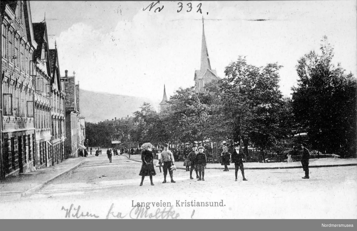 Postkort: 89986 ";Langveien Kristiansund";. Foto Langveien på Kirkelandet i Kristiansund , hvor vi ser deler av parken og Kirkelandet kirke i bakgrunnen på Lyshaugen. Ellers så ser vi en gruppe barn i forgrunnen ute i veien. Postkortet er utgitt av H. Tollevaens Forlag, og er trolig datert mellom 1905 og 1920. Fra Nordmøre Museums fotosamlinger. Reg: EFR
