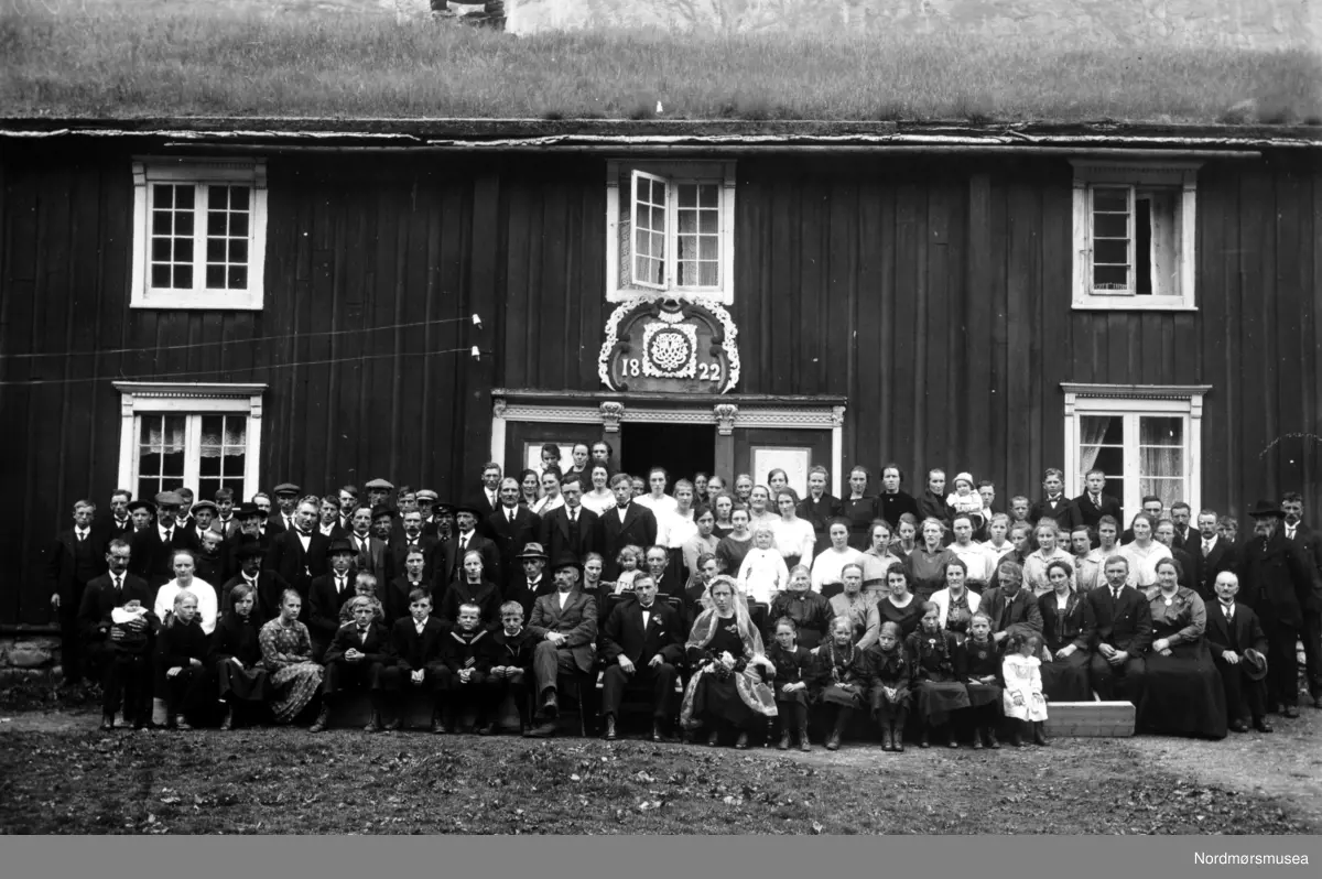 Foto av et bryllup på Åker i Sunndal kommune. Wedding of Anne Ingebrigtsdatter (Wennevold) Hoås (1893-1976) and John Ivarsen Hoås (1891-1972), in 1921. I believe at Wennevold, June 1921. (Info fra Brandon Henderson 2018)  Merk dørpryden med årstallet 1822 innskrevet.  Se også reg. nr. KMb-KMb-2007-007.0085 samt KMb-2007-007.0084. Fra Nordmøre Museums fotosamlinger.