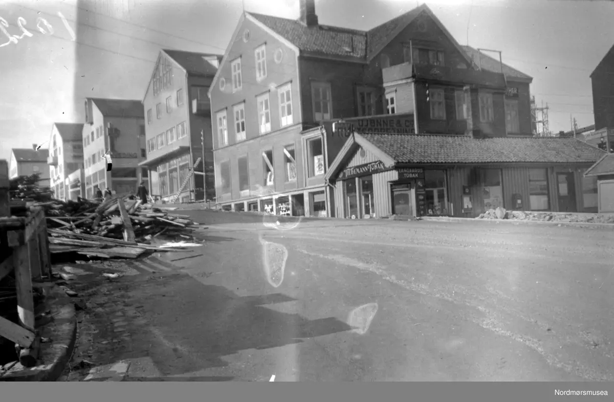 Loennechen gården ved Kaibakken, fotografert 27. mars 1949, en tid før dens nedriving, for å gi plass til det nye rådhuset. "Basarbygningen" med Øien's tobakksforettning på hjørnet, og baker Sivertsen (SIBAS) brødbutikk i forgrunnen lengre i nord, har ennå ikke flyttet ut. De siste leietakerne per 27. mars 1949, hvor flere er flyttet ut, var følgende: Kjelleretasjen: i sydenden O. Sandnes sko & lærhandel og i nord; Kafe Fosna, som var eid av Fru Eidsvåg. I gamle dager var dette Marit Fladvads kjente kaffestue. 1. etasje: i syd Hoems bokhandel, tidligere Barman og Heinrich Loennechen's bokhandel. Mot vest, og mot Lindahls plass, lå Wangbergs tobakk- og leketøysforettning. Solbjørs ramme- og glassforretning, Astrup & co's jern-varehandel. 2. etasje: i nord, Tannlege Selmer som fremdeles per 1949 har lokale her, videre doktor Sæther og tannlege Frislid. 3. etasje: Overrettssaksfører Marstrand, med kontor og privatbolig. Han var dessuten bestyrer av gården. "Kjernen" i gården går helt tilbake til 1780; den såkalte Helsinggården. Navnet er beholdt, skilt pr 2007. Nordmøre Museum