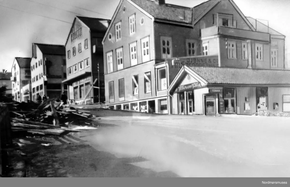 Loennechen gården ved Kaibakken, fotografert 27. mars 1949, en tid før dens nedriving, for å gi plass til det nye rådhuset. "Basarbygningen" med Øien's tobakksforettning på hjørnet, og baker Sivertsen (SIBAS) brødbutikk i forgrunnen lengre i nord, har ennå ikke flyttet ut. De siste leietakerne per 27. mars 1949, hvor flere er flyttet ut, var følgende: Kjelleretasjen: i sydenden O. Sandnes sko & lærhandel og i nord; Kafe Fosna, som var eid av Fru Eidsvåg. I gamle dager var dette Marit Fladvads kjente kaffestue. 1. etasje: i syd Hoems bokhandel, tidligere Barman og Heinrich Loennechen's bokhandel. Mot vest, og mot Lindahls plass, lå Wangbergs tobakk- og leketøysforettning. Solbjørs ramme- og glassforretning, Astrup & co's jern-varehandel. 2. etasje: i nord, Tannlege Selmer som fremdeles per 1949 har lokale her, videre doktor Sæther og tannlege Frislid. 3. etasje: Overrettssaksfører Marstrand, med kontor og privatbolig. Han var dessuten bestyrer av gården. "Kjernen" i gården går helt tilbake til 1780; den såkalte Helsinggården. Navnet er beholdt, skilt pr 2007. Nordmøre Museum
