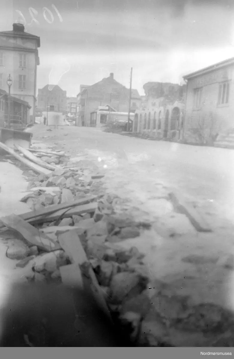 Bilde fra Skolegata, fotografert fra øst en dag i oktober 1948. Vi ser Festiviteten i bakgrunnen, med litt av den Høgre skole til venstre. Fra høyre ser vi Sparebankens barakke, ruinene til Hjemmenes vel som er fjernet per 23. april 1949, da det skal reises et nytt bygg der. Sakfører Per Ditlev Fayes kontorbarakke, Kafe Kristiansunds nybygg og deretter den nye Fastinggården - også advokat. Nordmøre Museums fotosamling. dublett.