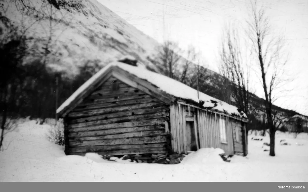 "Grønsetstua". Et vinterbilde med ei røykovnstue fra Gården Grønset på Gjemnes, hvor vi ser gavlvegg og langvegg som er laftet og panelt. Stua står nå på Gamle Kvernes Bygdemuseum. En avdeling av Stiftelsen Nordmøre Museum. Fra Nordmøre Museums fotosamlinger.