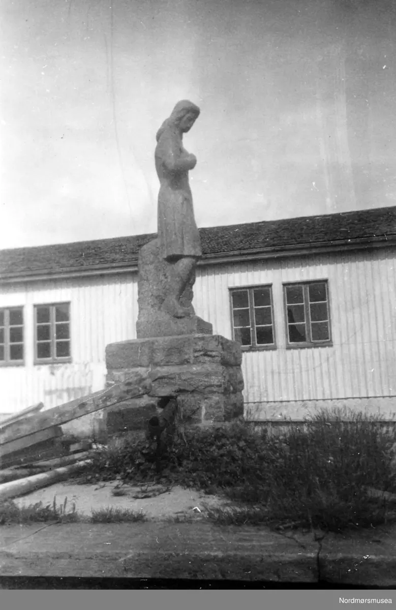 Nordre fløy av Soldatheimen med statuen i forgrunnen, i Lars Guttorms gate - nær Allanengen Skole. Statuen er utført av en tysk soldat ved navn Rainer, og forestiller en ung kvinne. Rainer, som var steinhugger og treskjærer i det sivile, laget statuen i en brakke i Vågen. Et vakkert kunstverk.
Etter 1945 ble bygningen solgt til Kristiansund Arbeiderparti, som til per dags dato (august 1955) har brukt lokalet som samlingssted, møtelokale, samt til utleie for byens forskjellige foreninger. Det har også blitt brukt til offentlig valglokale (den store salen). I disse dager (per august 1955) holder de på å rive Soldatheimen, for å gi plass til byggetomter. (Metodistkirken). Kilde (blant andre): Tidens Krav, Fredag 14. september 2007, side 20

";Stein Bach påsto at det var to slike statuer, den største stod utenfor "Soldatheimen" og en mindre sto inne i vestibylen. Han kunne fortelle at den største som ble knust og fraktet sammen med mer stein derifra til plassen uten for huset til far til Stein (Mellomveien 7 på Steinberget), da brukt som fyllmasse (noen påstår at dette ikke er riktig og det var bare en statue). Den gjenværende statuen står i hagen til tidligere byingeniør Røkkum. Den står der fremdeles. Det er i bakhagen til det øverste huset i Omveien. Du kan se den fra Nord-østliste delen av Kringsjå. Når du går fra Omveien opp til Kringsjå så ser du den til høyre."; Ut i fra dette så er den kanskje lagt ned under parkeringsplassen i Mellomveien, men det er ikke sikkert den er hel.



Bildet er fra Nordmøre Museums fotosamlinger.
