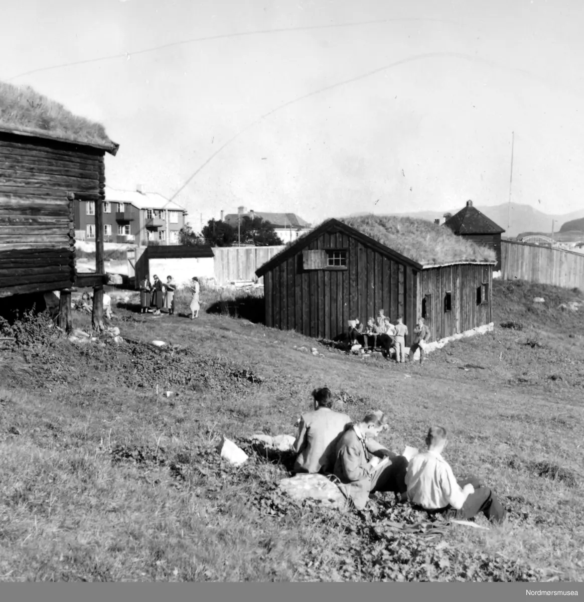 Almskårstua i Clausenenga før flytting til Knudtzondalen.
Røykstua (midten), litt av stabburet til venstre og "Vardetårnet fra 1808" i bakgrunnen.  Viser en studietur med frihandstegning og omvisning for en klasse av Kristiansund offentlige høyere allmenskole.  En varm og soleklar septemberdag.
(Frå Nordmøre Museum si fotosamling) duplikat