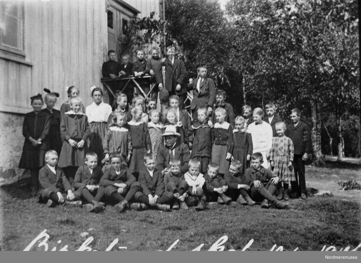 Skolebilde fra gamle Birkelund skole.  Nils Bjerkestrand var sløydlærer og står ytterst til høyre ved døren.  Tekst på fotoet:  ";Birkelund skole 10.6.1917.";  Skolen var per 1979 i bruk av Frei kommune.   Bilde fra fotoinnsamlinga i Frei kommune 1978-79. Innsamla og registrert av Freielever på Nordlandet ungdommskole. Fra Nordmøre Museum sin fotosamling.
Reg: EFR
