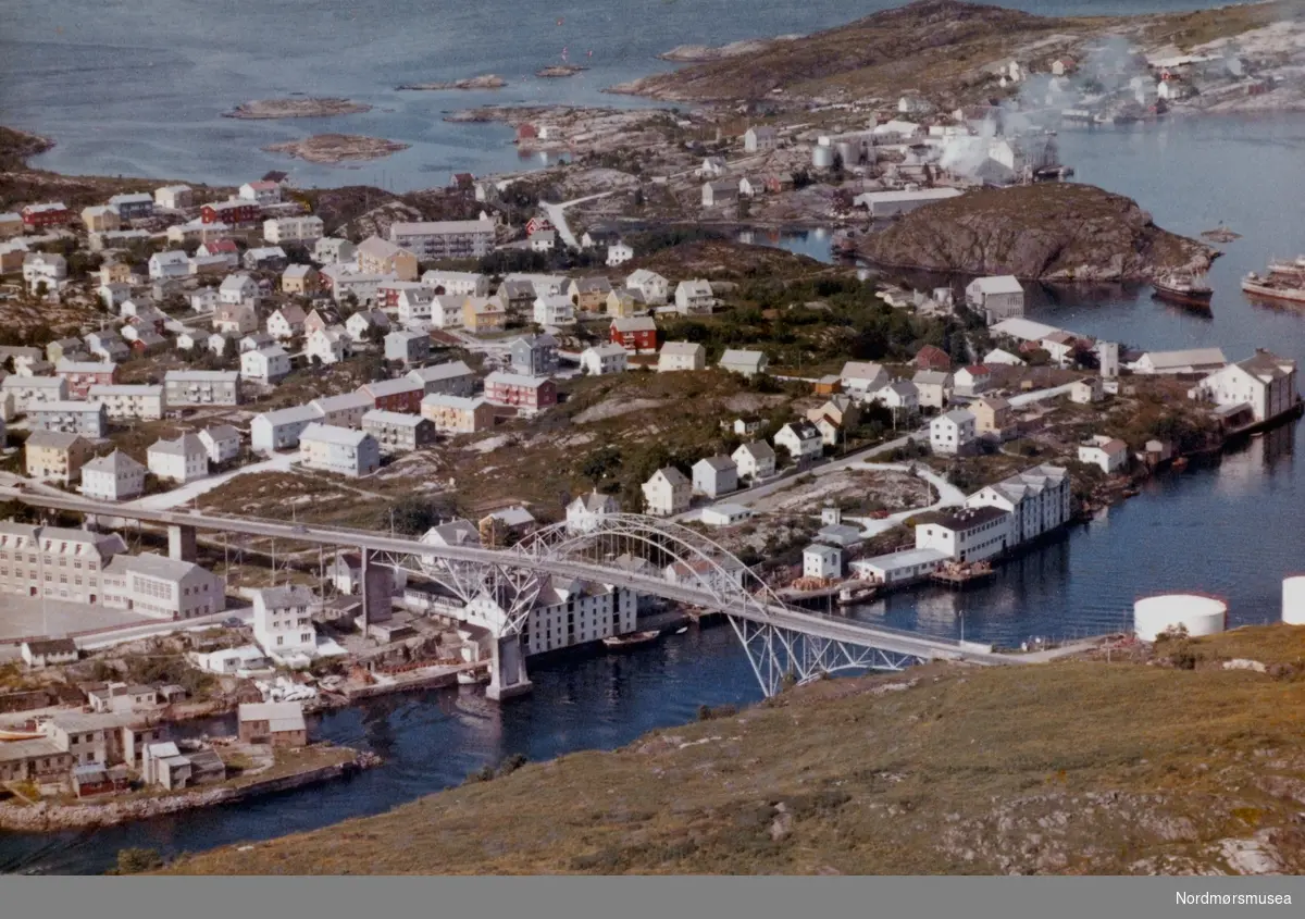 Flyfoto over Gomalandet i Kristiansund. Midt på bildet kan vi se Nordsundbroa, som var ferdigbygd i 1936, denne brua er pr 2008 revet og erstattet med en ny bro. Nederst på bildet til venstre kan vi se Nordholmen. Rett ovenfor Nordholmen kan vi se gamle Gomalandet Skole. Øverst på bildet hvor vi kan se industrirøyk er Bentnes Sildoljefabrikk. Datert 11 juli 1962.  (Fra Nordmøre Museums fotosamlinger)