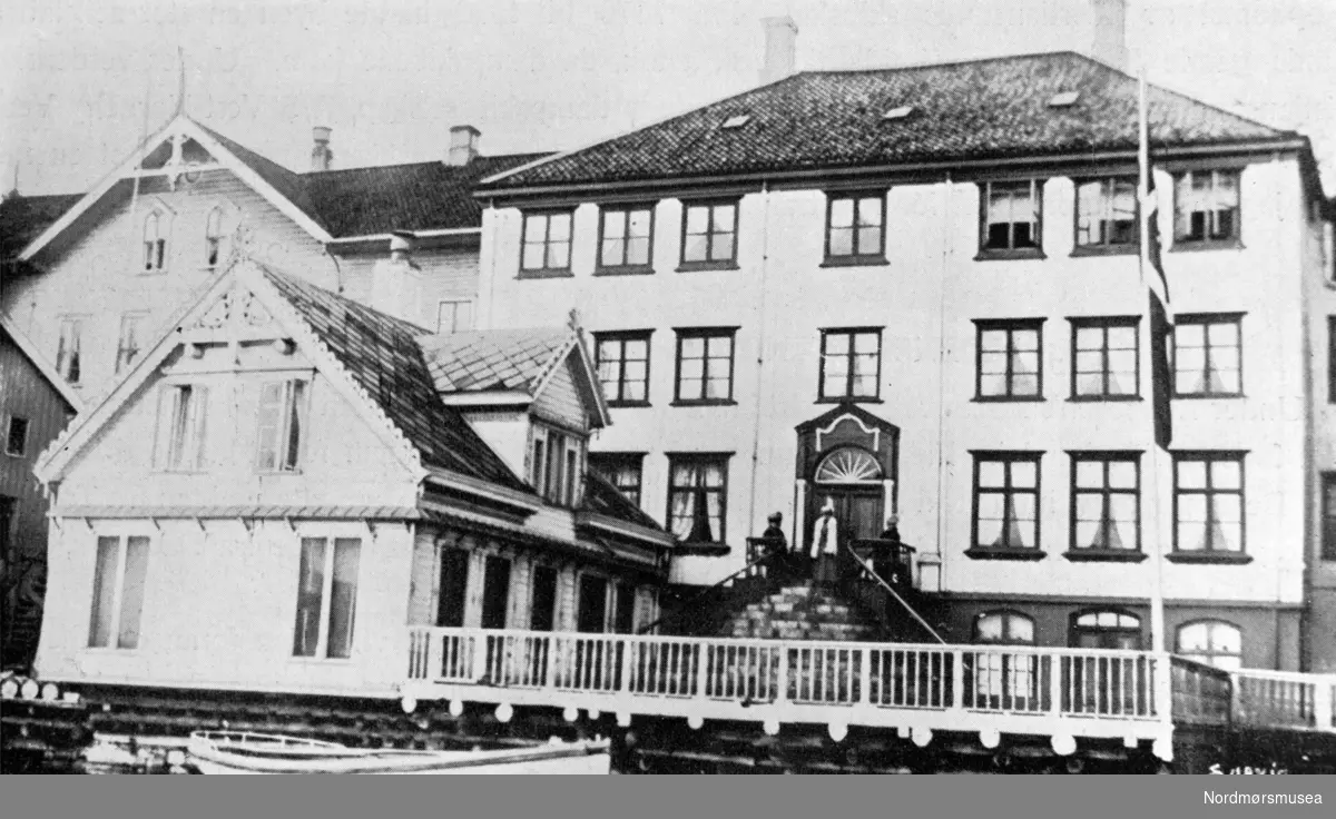 Knudtzongården nede ved havna på Kirkelandet i Kristiansund. Her sett fra hovedfasaden med kontoret til venstre. NB. Legg merke til flagget på halv stang. Dødsfall i familien?
Datering er trolig omkring 1928. Fra Nordmøre museums fotosamlinger.
