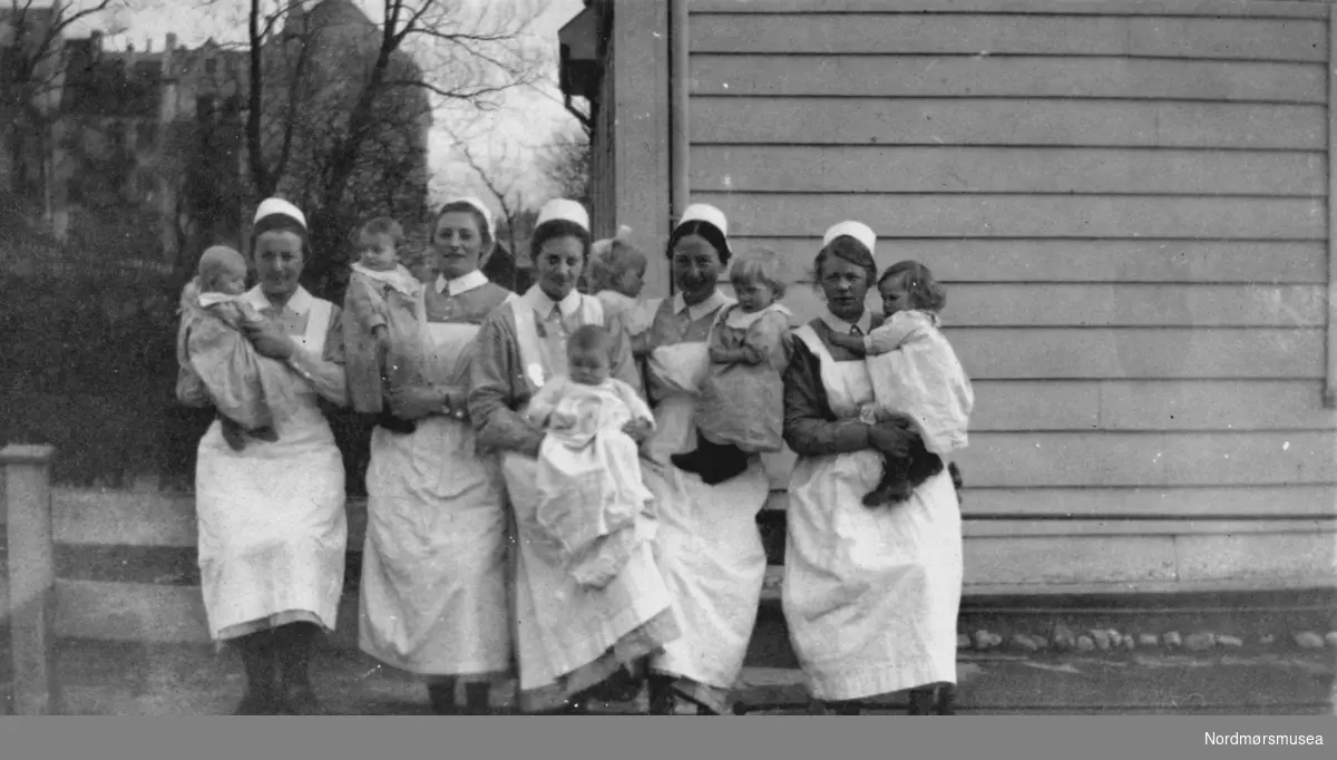 Foto av en gruppe sykesøstre/sykepleiere med hvert sitt spedbarn på armen. Ukjent hvor. Ved et barnehjem? Sykehus? Datering er også ukjent, men trolig omkring 1918 til 1919. Bildet ble gitt til Nordmøre museum av Nelly Rødsand 5. september 1983. Fotoalbumet består av bilder med reg. nr. KMb-1983-024.0049 til KMb-1983-024.0223. Flere bilder fra andre album er å finne på samlingsnummer KMb-1983-024. Fra Nordmøre museums fotosamlinger.



