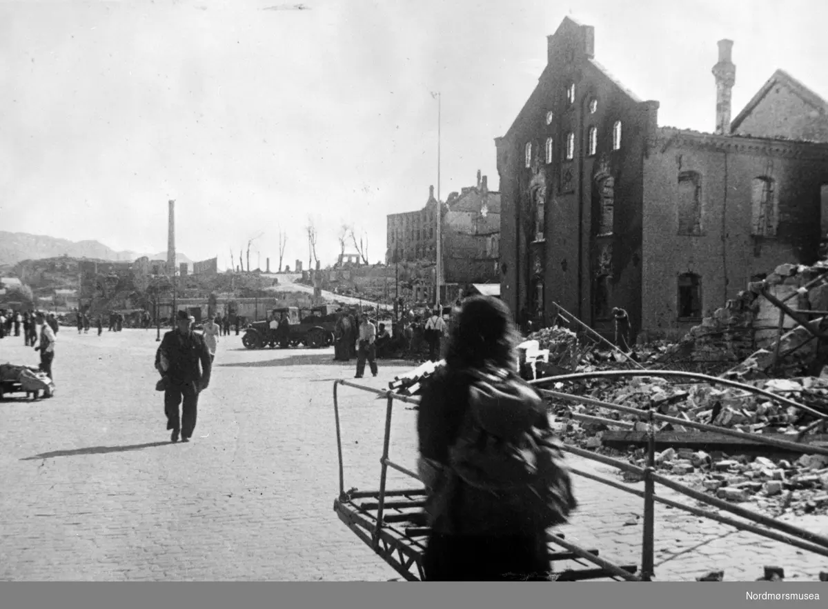 Krigen har kommet til Kirkelandet i Kristiansund. Etter nazistenes herjinger i perioden 28. april til 1. mai 1940 ligger nå store deler av byen i ruiner. Dette bildet viser fra området ved havna, fisketorget med fisketrappa og ruinene av bla.a. tollboden som vi ser på høyre side.

Etter bombigen løp det totale antall brente bygg på tilsammen 767, hvor 605 av disse var på Kirkelandet og 162 på andre ";land"; i Kristiansund. Her fantes det til blant annet til sammen 3906 boliger ifølge boligtellingen av 1938, og av disse brant 2162 boliger ned og 7099 mennesker ble husløse. I tillegg til de 767 brente byggene brant 36 fiskepakkehus ned til grunnen, hvorav 34 lå på andre ";land";. Verdien av de brente byggene beløp seg til kroner 26,9 millioner for Kirkelandet (kroneverdi per 1940) eller tilsammen 30,6 millioner kroner (kroneverdi per 1940) for hele byen. Fra Nordmøre Museums fotosamlinger. Kilde: Gjenreisningsproblemer i Kristiansund. Fremlagt ved gjenreisningsinstituttet i Kristiansund. Juli 1945. Side 16 - 20.
