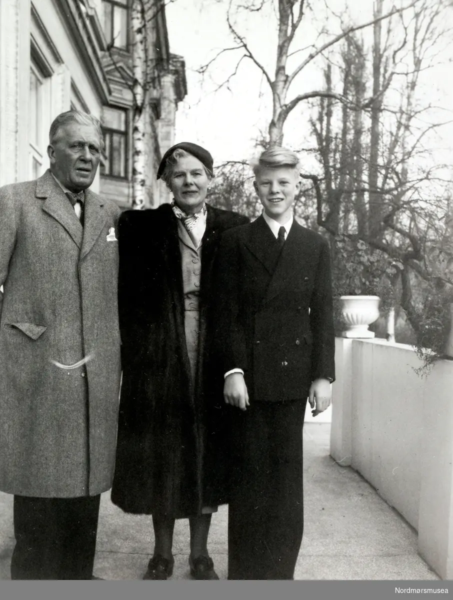 Foto trolig av far, mor og sønn Tjersland. Mannen til venstre kan da muligens være Alf Tjersland. Dette er basert på en tom konvolutt som fulgte med Fastingfamiliens samling, hvor avsenderens adresse er oppført med Alf Tjersland, Oslo. Incognitogaten 11. Ettersom dette bildet har gaten Incognitogaten 11 påskrevet på baksiden, antar jeg at dette da kan være familien Tjersland. Det er ellers påført teksten Dec. 61953 på bildet. Kan dette bety 6 December 1953? Sannsynligvis. Fotoserie. Fotografier gitt til Nordmøre Museum fra Kate og Kristian Fastings arvinger per 1986. Fra Nordmøre Museums fotosamlinger.
