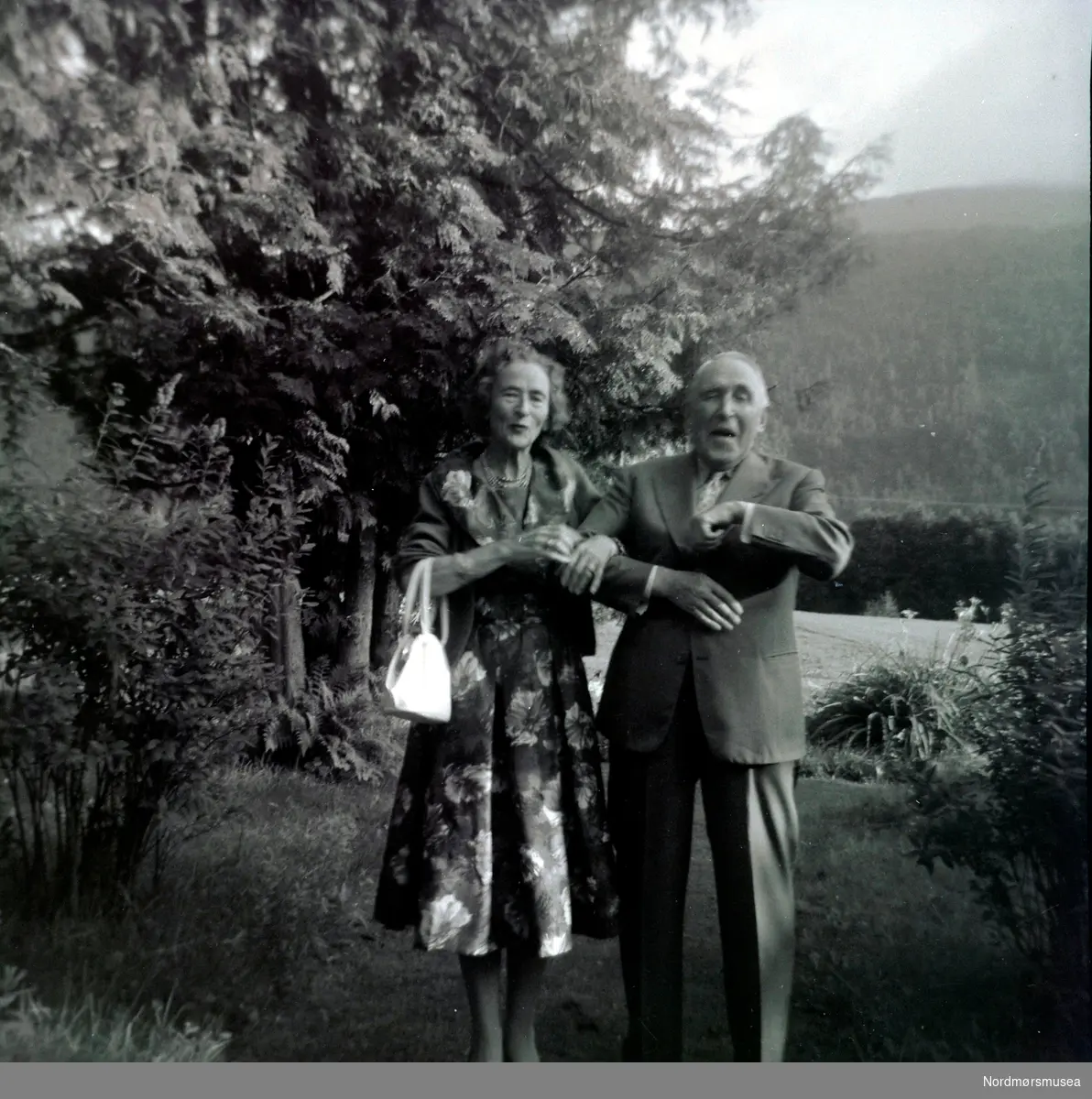 Foto av et eldre ektepar ute i naturen. Trolig fra slekten Fasting, eller fra deres omgangskrets. Ukjent fotograf (Fasting?), sted og datering. Fotoserie. Se også reg. nr. KMb-1986-013.0015. Fotografier gitt til Nordmøre Museum fra Kate og Kristian Fastings arvinger per 1986. Fra Nordmøre Museums fotosamlinger. 