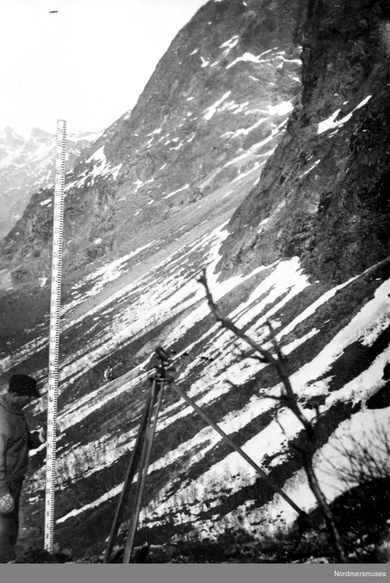 Landmålerutstyr ifm veibygging i Hallarvasslia,  mest trolig. Fjellfoten av Gammelurkollen i bakgrunnen.
(info: Terje Linseth) - Gammelurkollen 1.384 meter over havet.  landmålerkikkert. teodolitt. måler snøfonndybde ? 1930-50. Fra Nordmøre Museum sin fotosamling.