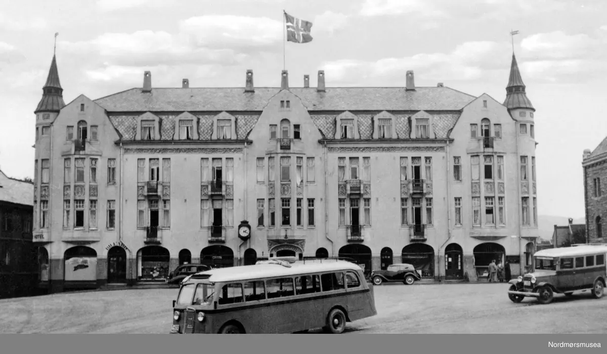 Et bilde av byens andre Grand Hotell. Byens første Grand Hotell var bygd i sveitserstil, men 8. november 1907 brant dette ned til grunnen. Eieren av hotellet Nils Nilsen valgte senere arkitekt Kr. T. Rivertz fra Kristiania til å bygge opp hotellet. Rivertz oppholdte seg da i perioden 1907-1909 i Kristiansund, hvor han blant annet har tegnet "Badet";, Festiviteten, Grand Hotell og Norges banks lokaler i samme gaten som Grand Hotell. Hotellet ble oppført av murmesterfirmaet Olsen & Michalsen i Jugendstil, og under Rivertz' ledelse og tegninger. Hotellet kostet litt over 200.000 kroner å bygge, men summen inkluderer ikke tomten og monteringen (Referanse: En oplevelsens festlabyrint av Egil Husby, side 15 - 17). Byens andre Grand Hotell brant under bybrannen 28. april 1940, da tyskerne brente store deler av Kirkelandet ned til grunnen. Leonard Hjelle kunne i 1936, etter åpningen av Nordsundbrua mellom Gomalandet og Nordlandet, sette i gang ringbussrute i Kristiansund. Her ser vi to av bussene på Torvet. 
Fra Nordmøre Museums fotosamlinger. 

Fremre buss kan være en International C-serie 1934-36/37 bulldog, fulgt av Studebaker 1932 reg. på. T-4274 med karosseri av Johs. Olsen, Tronheim.
 (Tilleggsinfo: Ivar E. Stav.)



 Den fremste bussen er saynnsynligvis T-4232 International C35B 1935-modell. Karosseriet var bygd hos Brødrene Berg på Byneset i Trondheim. Bussen hadde 20 seter og Kristiansund-Oppdal Auto (KOA). Som ny gikk den i ruta Oppdal--Kristiansund. Hvis den bakre bussen er T-4274 så var også det en buss som tilhørte KOA. Før 1938 var det  KOA og Surnadal Billag som hadde ruter til og fra Kristiansund foruten Ringbussen i Kristiansund. I 1932 åpnet ferjesambandet Kvisvik-Kristiansund og bussene fulgte ferja fram til Kristiansund sentrum. I 1938 åpnet ferjesambandet Gjemnes-Kristiansund, og dermed fulgte rutevogner fra Molde og Batnfjorden ferja til Kristiansund. (mer info fra Sveinung Berild - 07.10.2016)