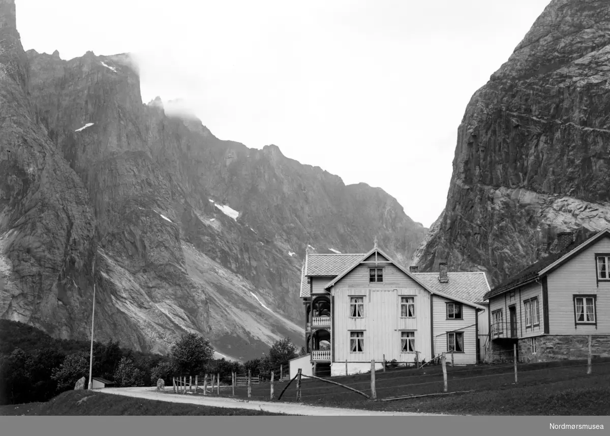 Dette er fra Horgheim Skysstasjon på Horgheim i Romsdalen, Rauma kommune. Husa er noe oppussa, og står 2019 fortsatt slik som på bildet. Når vi ser på vegen, er nok bildet tatt nærmere 1930.  Fjellet bak til venstre er Trollveggen. Bak der igjen er Trolltindene, med Store Trolltind som høyest. 1788 moh. (E. Sæbø). 
Fra Nordmøre Museum sin fotosamling. serie