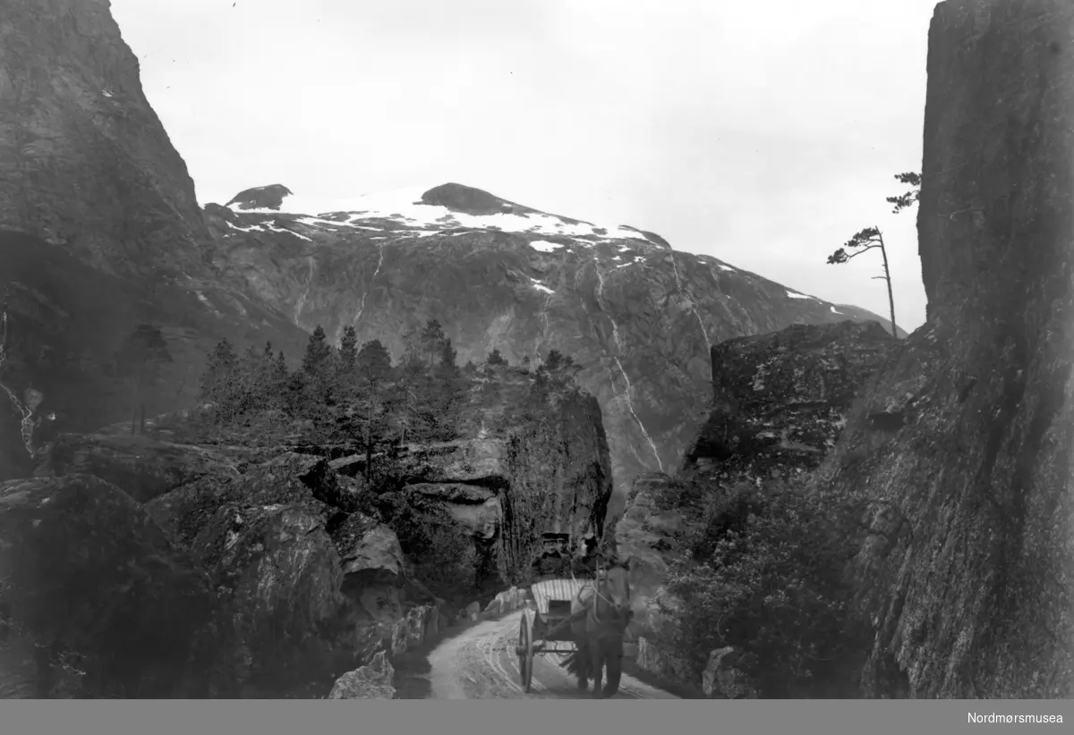 Tekst mangler. Her trenger vi hjelp av noen som kjenner seg igjen. Hvor, når, hvem er avbildet? Hesteskyss i Drivdalen?
 Kan det være nede i Drivdalen før stigningen? Fra Nordmøre Museum si fotosamling
