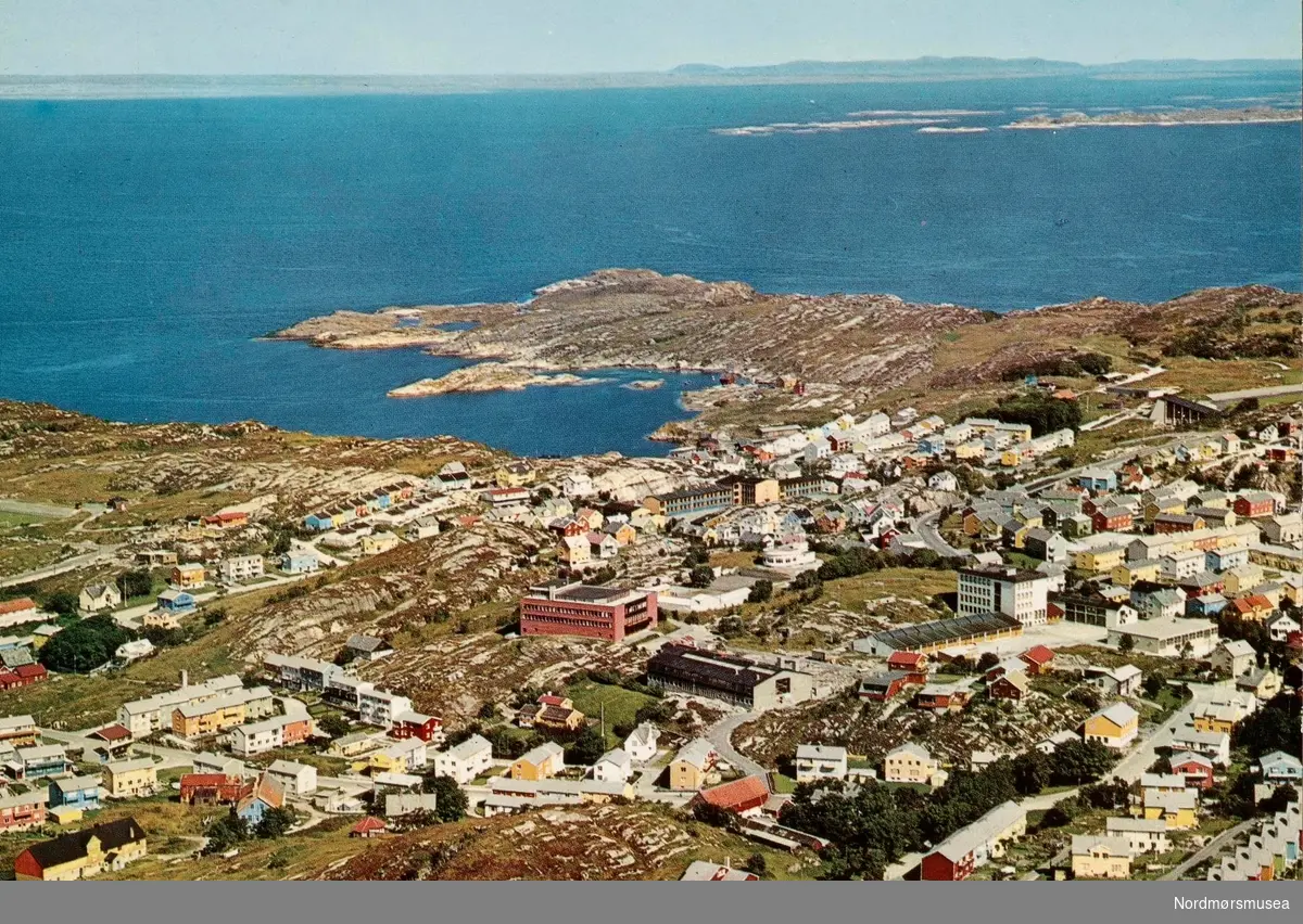 Postkort "F-2860-6" med motiv fra området ved St. hanshaugen vdg. skole (nå Kristiansund vdg. skole) på Kirkelandet i Kristiansund, med et skolebygg i rød murstein midt på bildet. Ennå så er ikke "blåbygget" blitt oppført. Kortet er utgitt av Knut Aune kunstforlag A/S, ved Sverdrups Bokhandel A/S. Fra Nordmøre Museums fotosamlinger.