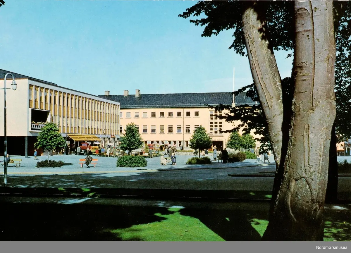 Postkort ";0120/3"; med motiv fra Kongens plass i Kristiansund. Her ser vi Folkets hus til venstre samt post- og telegrafbygningen i bakgrunnen. Foto er av Giovanni Trimboli. Fra Nordmøre Museums fotosamlinger. Reg: EFR
