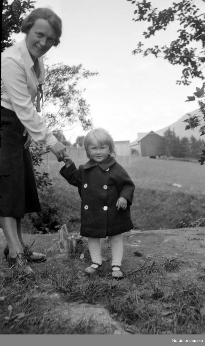 Kvinnen på bildet er Gudny Sverdrup, gift med Henrik Sverdrup, eldste sønn til Georg Sverdrup. Piken på bildet er sannsynligvis datteren Anne Lise. Bildet er tatt i Eidsvåg i Nesset kommun, Møre og Romsdal fylke. Datering er trolig omkring 1920 til 1939. Fra Nordmøre museums fotosamlinger.
