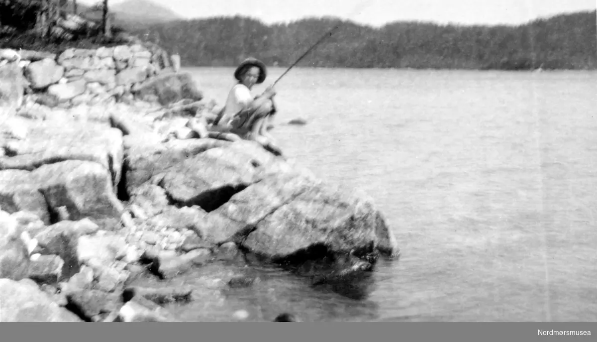 Foto av en gutt som sitter å fiske ved sjøkanten. Fra Nordmøre Museum sin fotosamling
