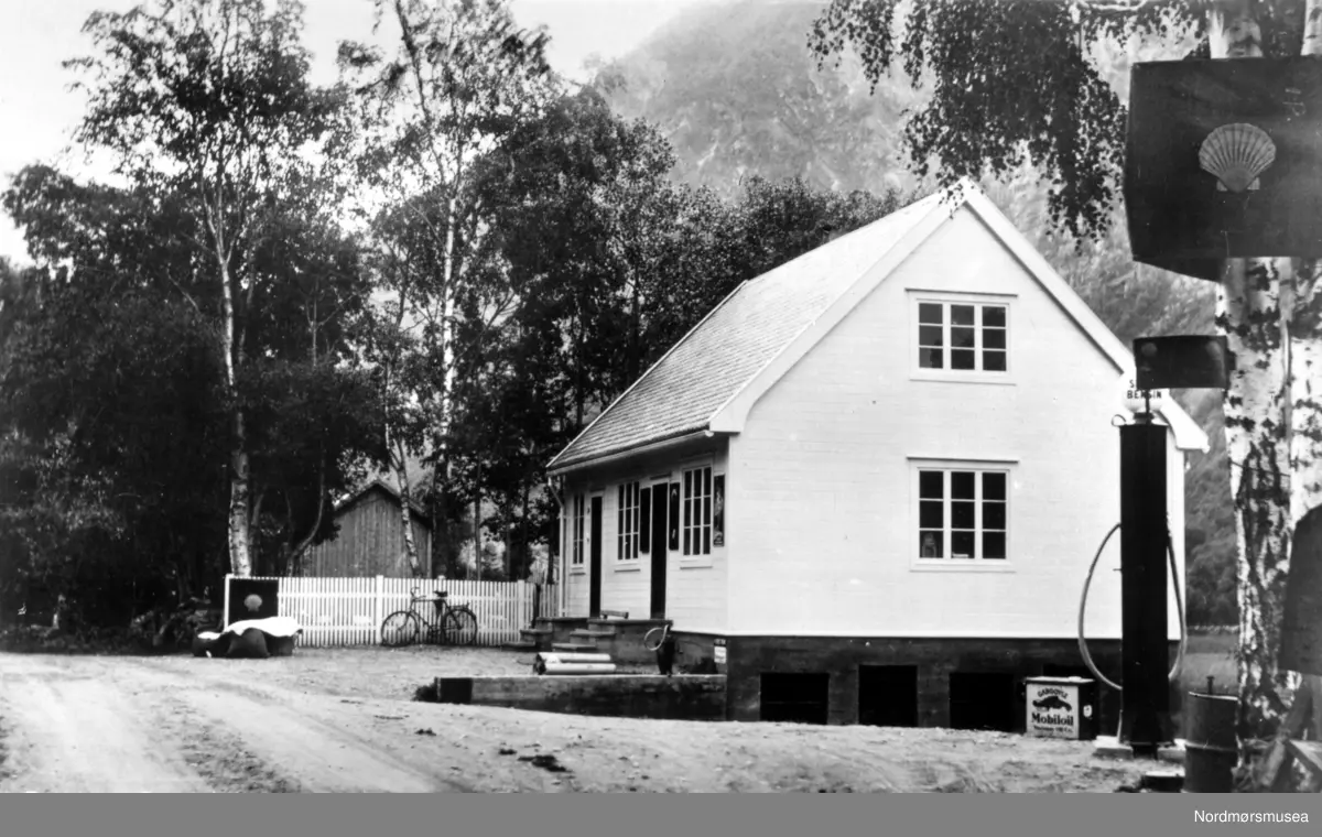 Dette er butikken til Lars Hansen Herskedal på Gravem. Huset ble revet etter at  en stein fra ura traff taket og gikk i gjenom. (Info: Harald Gravem 2017). En eldre Shell bensinstasjon på Gravem i Sunndal kommune. På bildet ser vi en bensinpumpe og Shell skiltet i forgrunnen, mens i bakgrunnen ser vi en sykkel. Mobiloil dunk. Fra Nordmøre Museum si fotosamling.