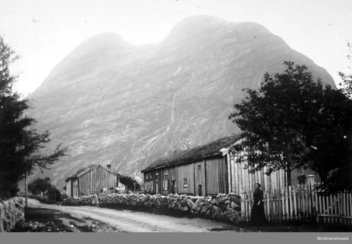 Foto fra en landevei, hvor vi ser fra gamle gårdshus i tømmer og med torvtak, ukjent hvor. Muligens i Sunndal kommune? Fotograf er trolig Georg Sverdrup. Datering er muligens omkring 1910 til 1930. Fra Nordmøre museums fotosamlinger. Reg: EFR
