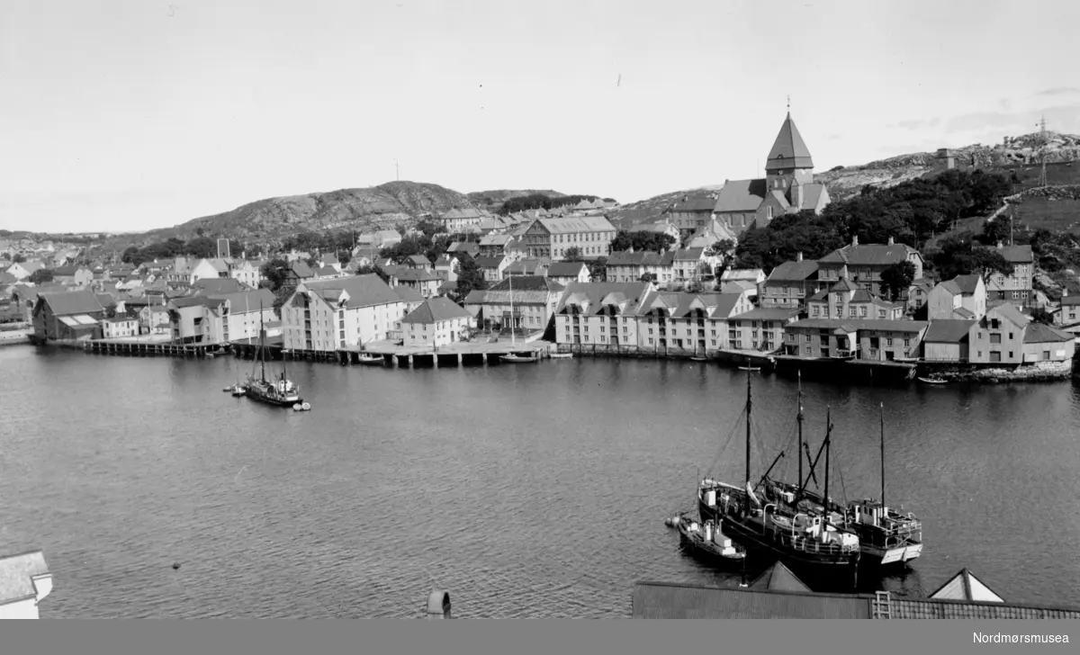 Foto sett fra Innlandet, hvor vi ser over sundet til Nordlandet, med Nordlandet kirke sentralt på bildet. Nede ved vannkanten ligger Pareliusgården og bryggene på rad og rekke, mens ute i Marcussundet ser vi flere båter. Bildet er trolig fra perioden 1935 til 1939. Fra Nordmøre Museums fotosamlinge.
