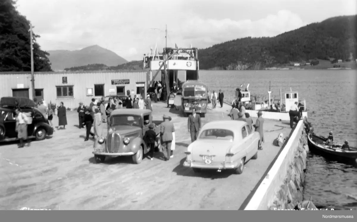 1938 Ford V8 lett lastebil, til høyre 1949-51 amerikansk Ford, bak 1946-47 Chevrolet buss.(Info: Ivar Stav 2018). - BIldet er nok tatt tidlig på 1950-tallet etter bilene å bedømme. Før øvring ble trafikken over Gjemnes ferjekai nedlagt i 1968 og overført til Høgset. Det forkortet ferjeturen til Kvitnes med noen få minutter. Ferjekaia på Gjemnes åpnet i 1938 med ferjerute i Kristiansund. Sommeren 1952 ble ferjeruta forkortet til Gjemnes-Kvitnes etter at veien over Frei var godt nok utbygd til å ta biltrafikken. (info: Sveinung Berild 2018). 


 -Postkort: Gjemnes. Enerett: Fridthjof Bruseth. Foto fra fergekaia i Gjemnes, hvor vi ser biler som er i ferd med å kjøre på land. Fra Nordmøre Museums fotosamlinger.