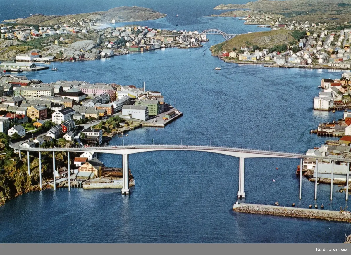 Postkort med flyfoto over Sørsundbroen som spenner mellom Kirkelandet til venstre og Innlandet til høyre i Kristiansund. I bakgrunnen ser vi Nordsundbroen som knytter Gomalandet til venstre og Nordlandet til høyre sammen.
 Datering er ukjent, men kan muligens være fra omkring 1970 til 1975. Utgiver er usikker. Samlingen av forskjellige postkort fra Kristiansund strekker seg fra KMb-1987-005.6103 til KMb-1987-005.6161. Fra Nordmøre museums fotosamlinger. /Reg:EFR2013/
