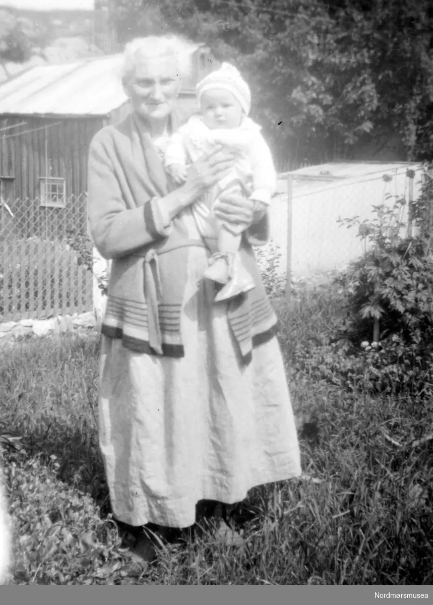 Foto av en ukjent kvinne med et barn på armen, trolig i Vistdalen i Nesset kommune. Fotograf er sannsynligvis et medlem fra Rød familien. Ukjent datering, trolig mellom 1920 til 1939. Giver av bildet er Turid Rød. Fra Nordmøre Museums fotosamlinger.