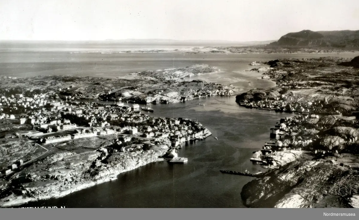 Postkort med tekst:  "KRISTIANSUND".
Luftfoto over Kristiansund som viser innflyving over Sørsundet med Kirkelandet  nærmest til venstre og Innlandet til høyre.  Videre inn ser vi Havna med Vågen og Gomalandet til venstre og Markussundet og Nordlandet til høyre.  Lengre bak ser vi Meløya og Skorpa til venstre, Nordsundet og Dalesundet midt i og Dale og Kvitneset til høyre.  I bakgrunnen ser vi Tustna med Jørgenvågsalen til høyre og  utenfor til venstre Langholmen.
 (Fra Nordmøre Museums fotosamlinger.)